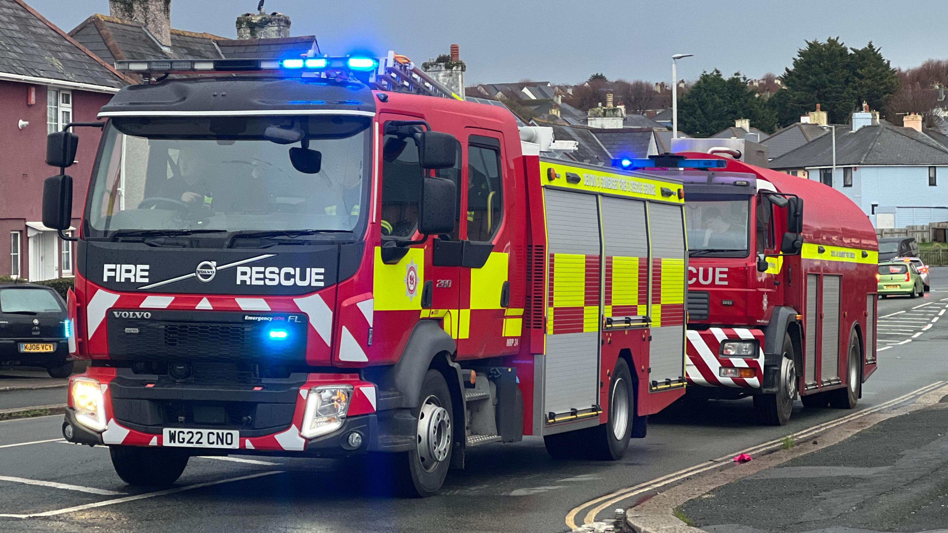 Two red white and yellow fire engines driving along the road. 