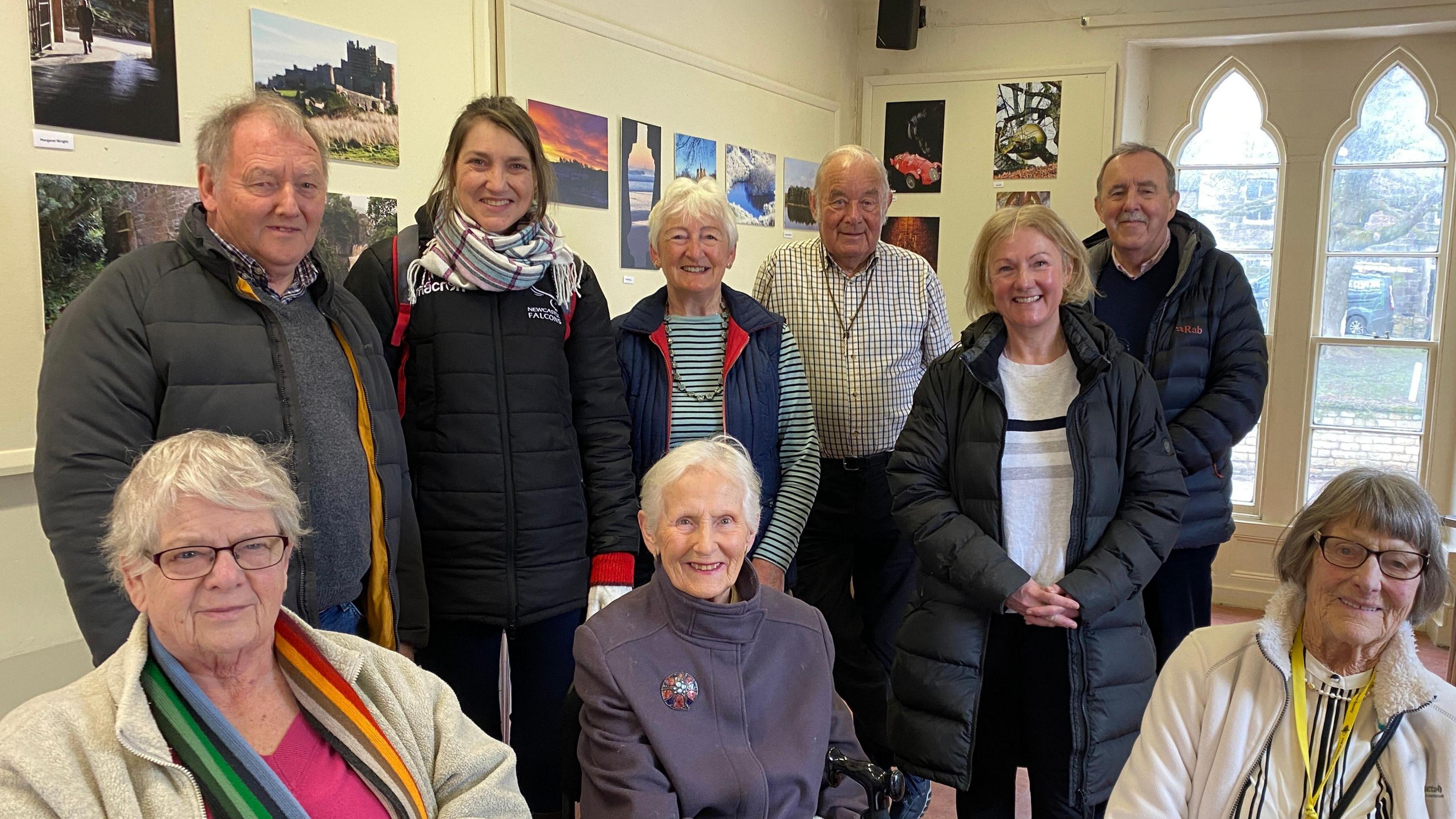 A group of people with photographs on the wall behind them 