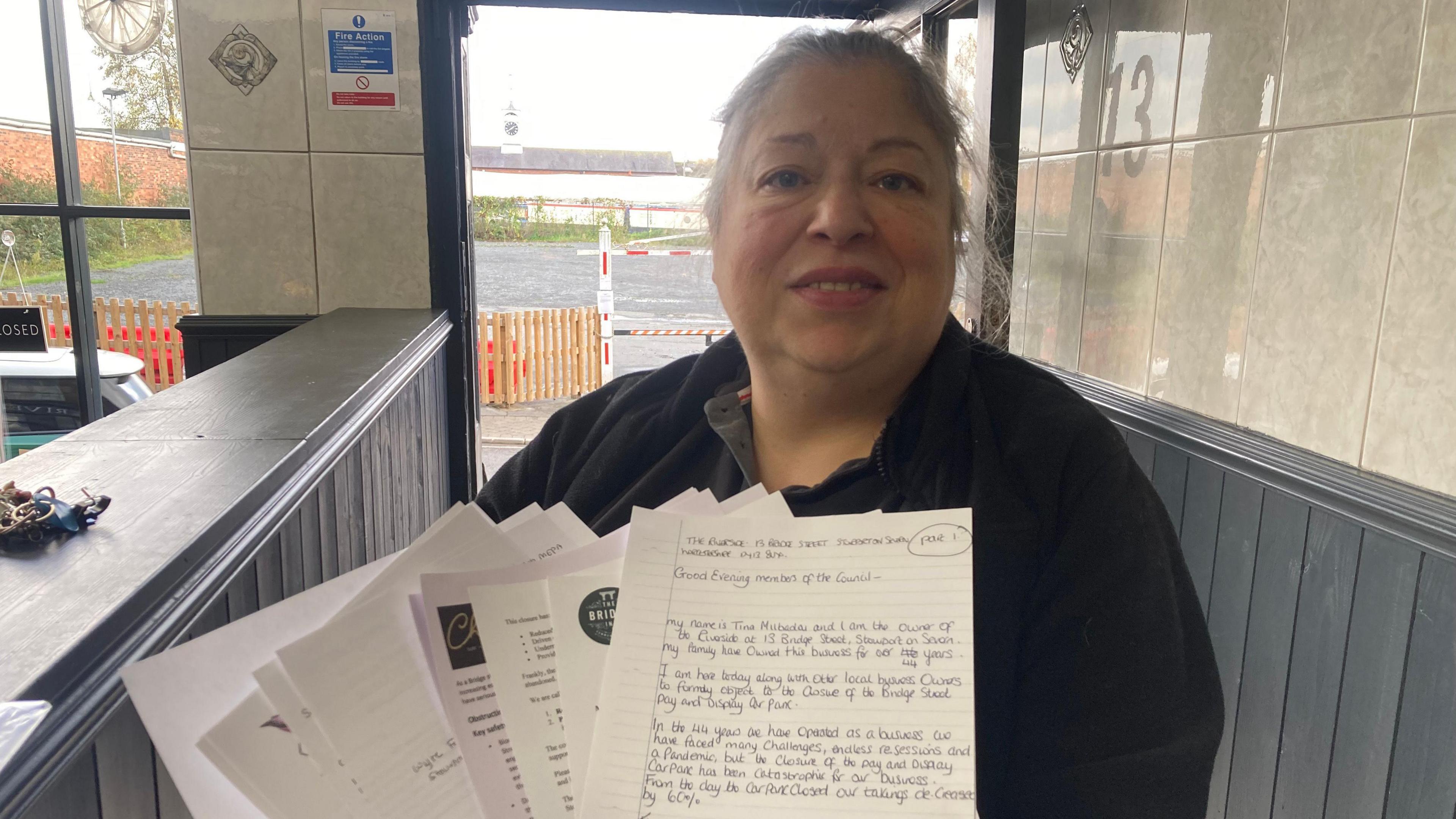 A woman stood inside a shop, holding up a series of objection letters.