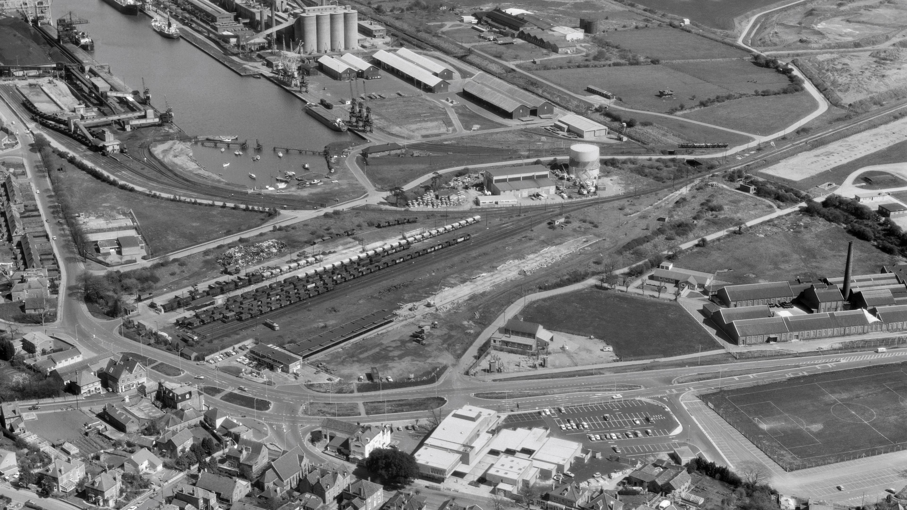 Old archive aerial shot of Portishead. There's the docks and power station around the water. There's a clear road going into the town and then a line where the railway track was.