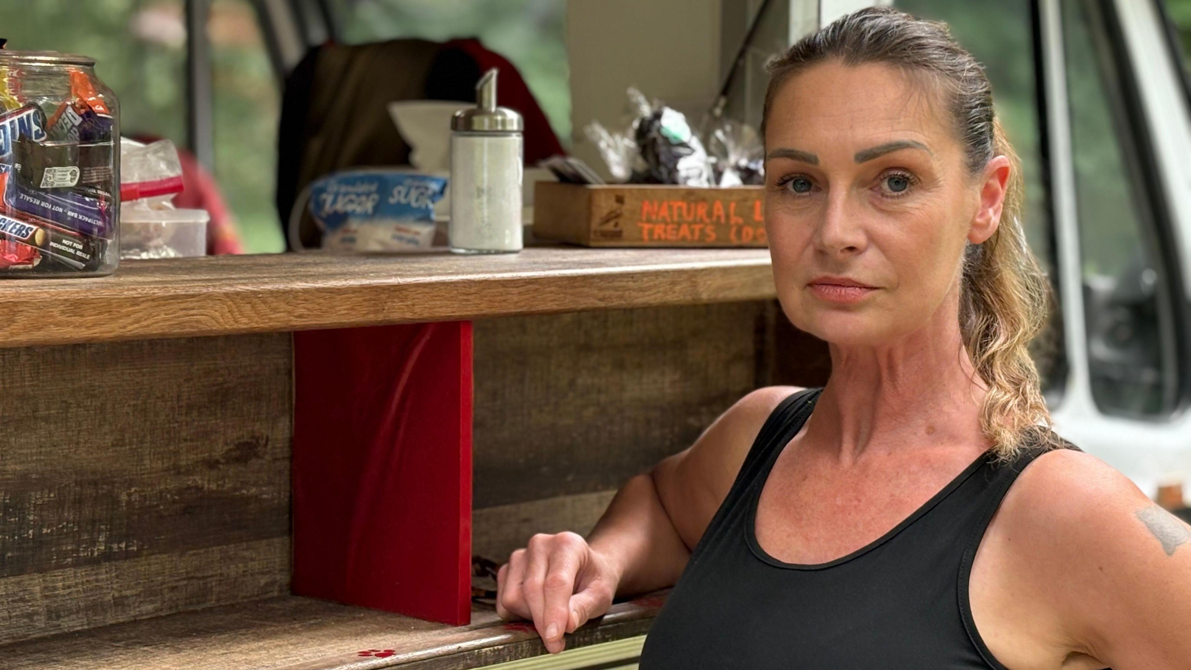 A woman in her 50's stands next to the kiosk of her food truck.