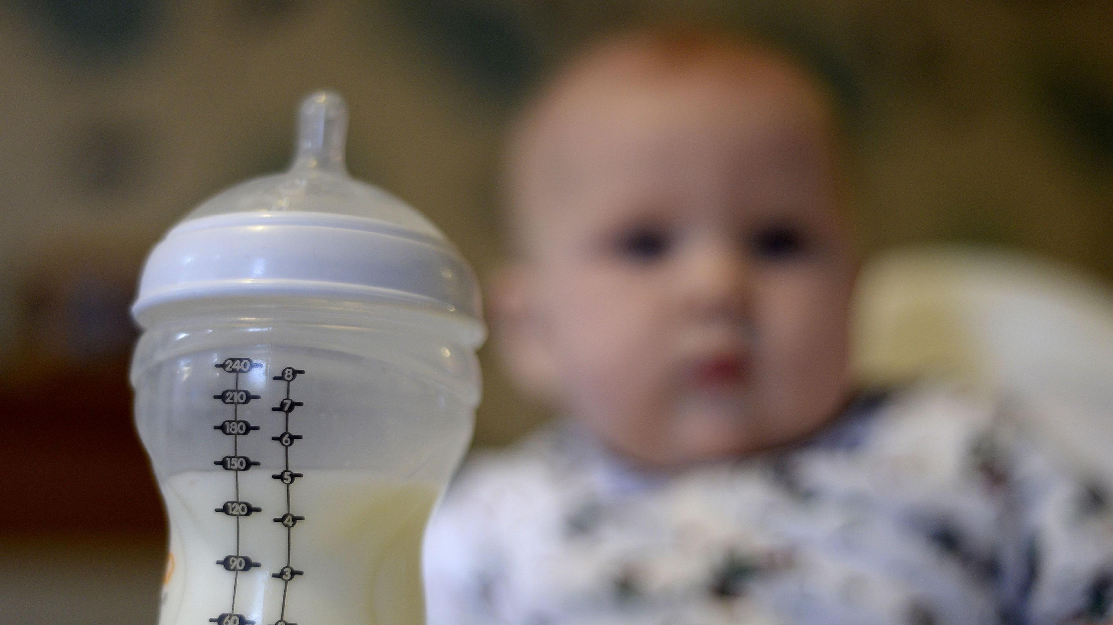 Image of a bottle of baby milk and a baby in its highchair 