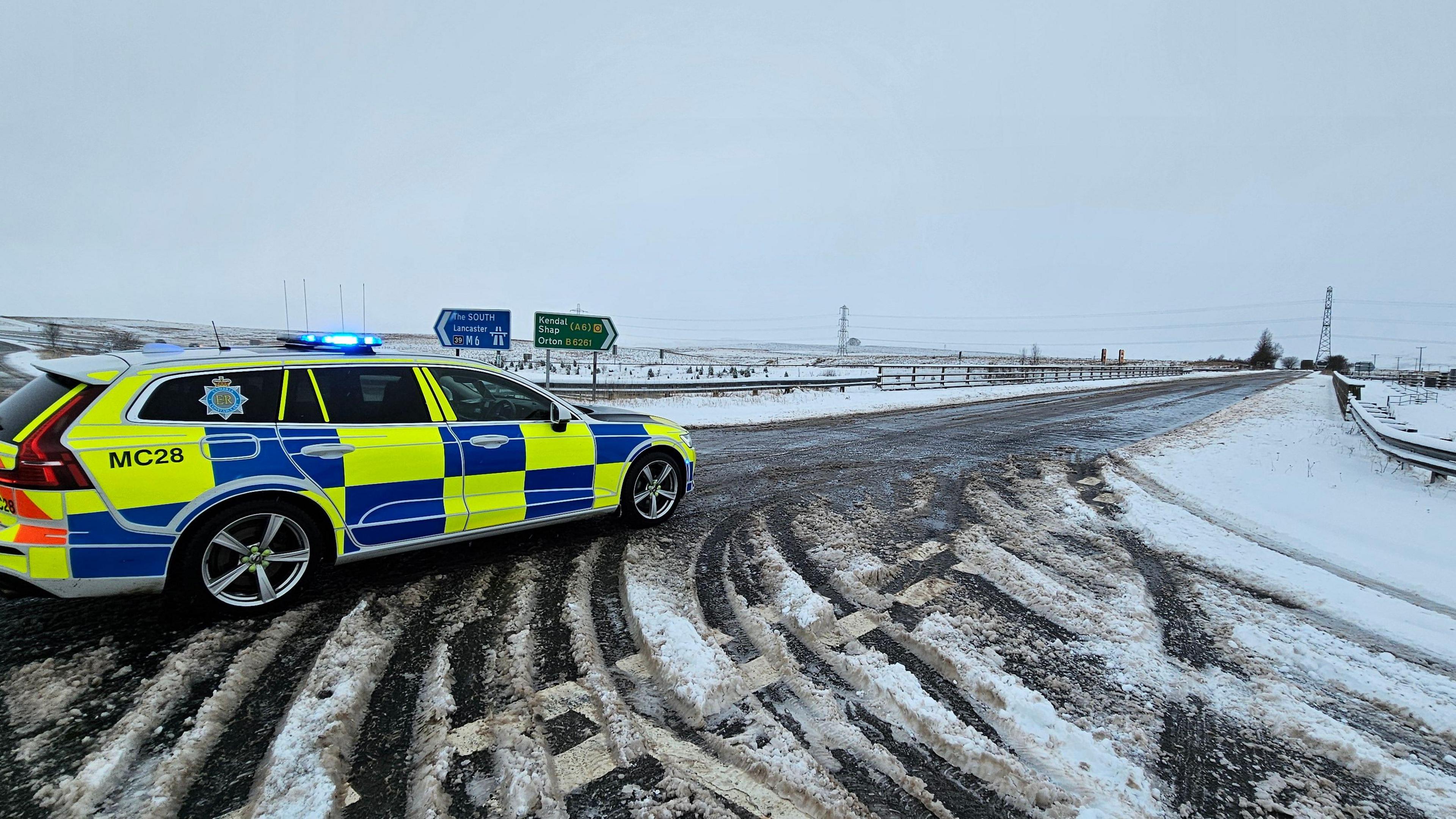 A Cumbria Police car with is blue lights on on a snowy road.