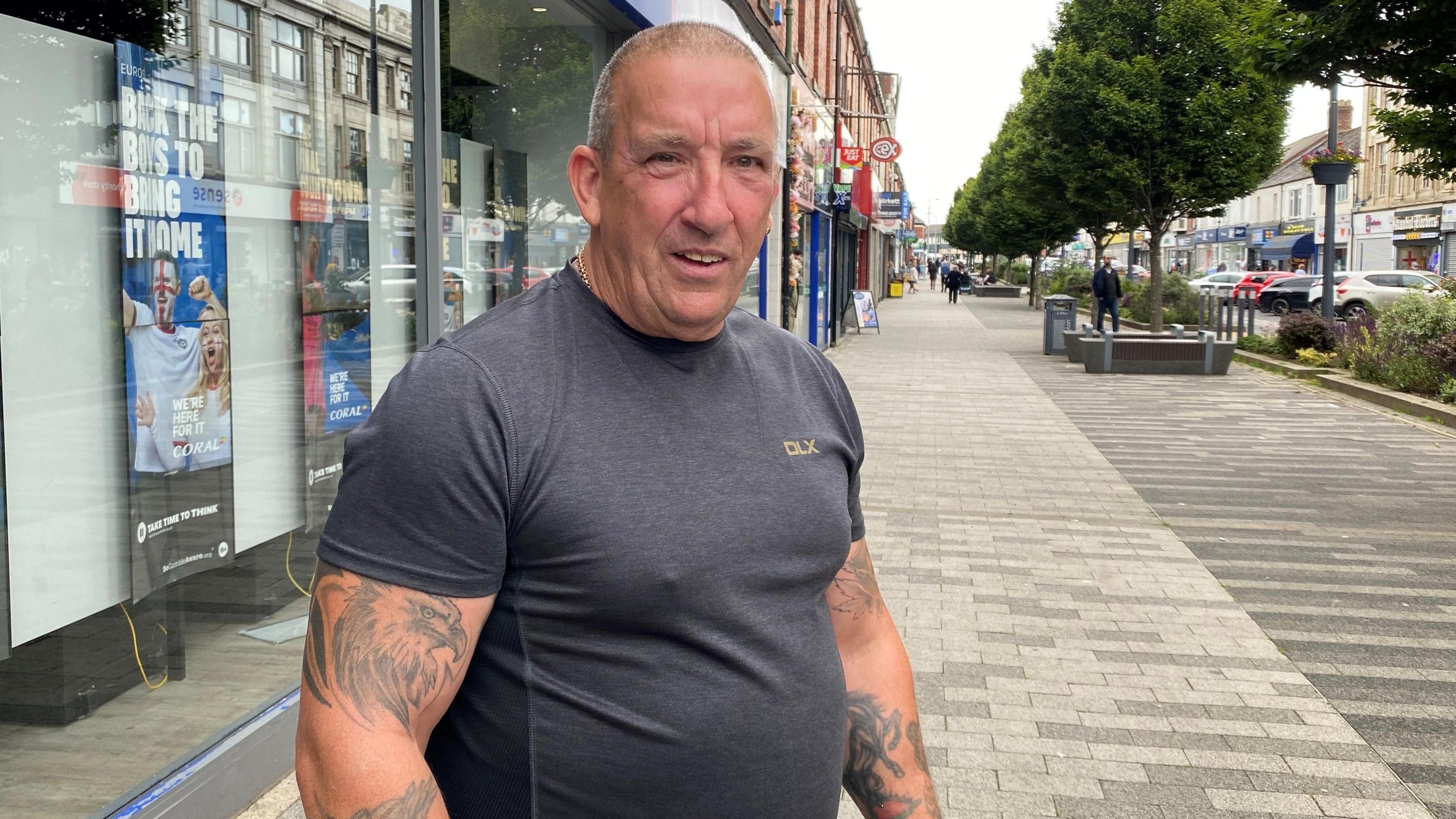 A man with lots of tattoos with Ashington high street behind 