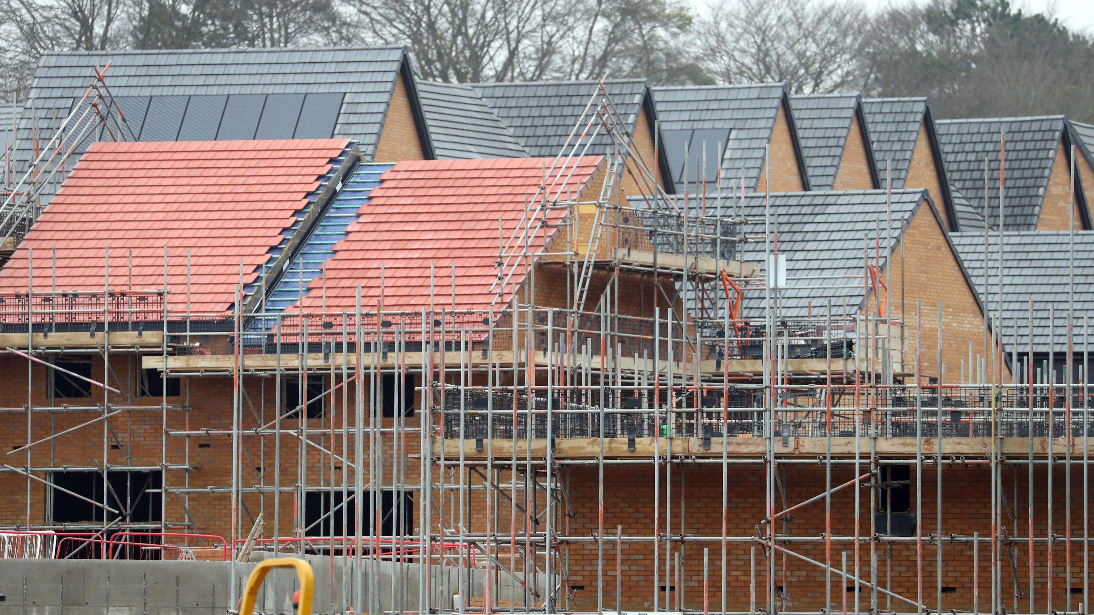 Construction being carried out on a housing development with scaffolding surrounding multiple houses nearing completion