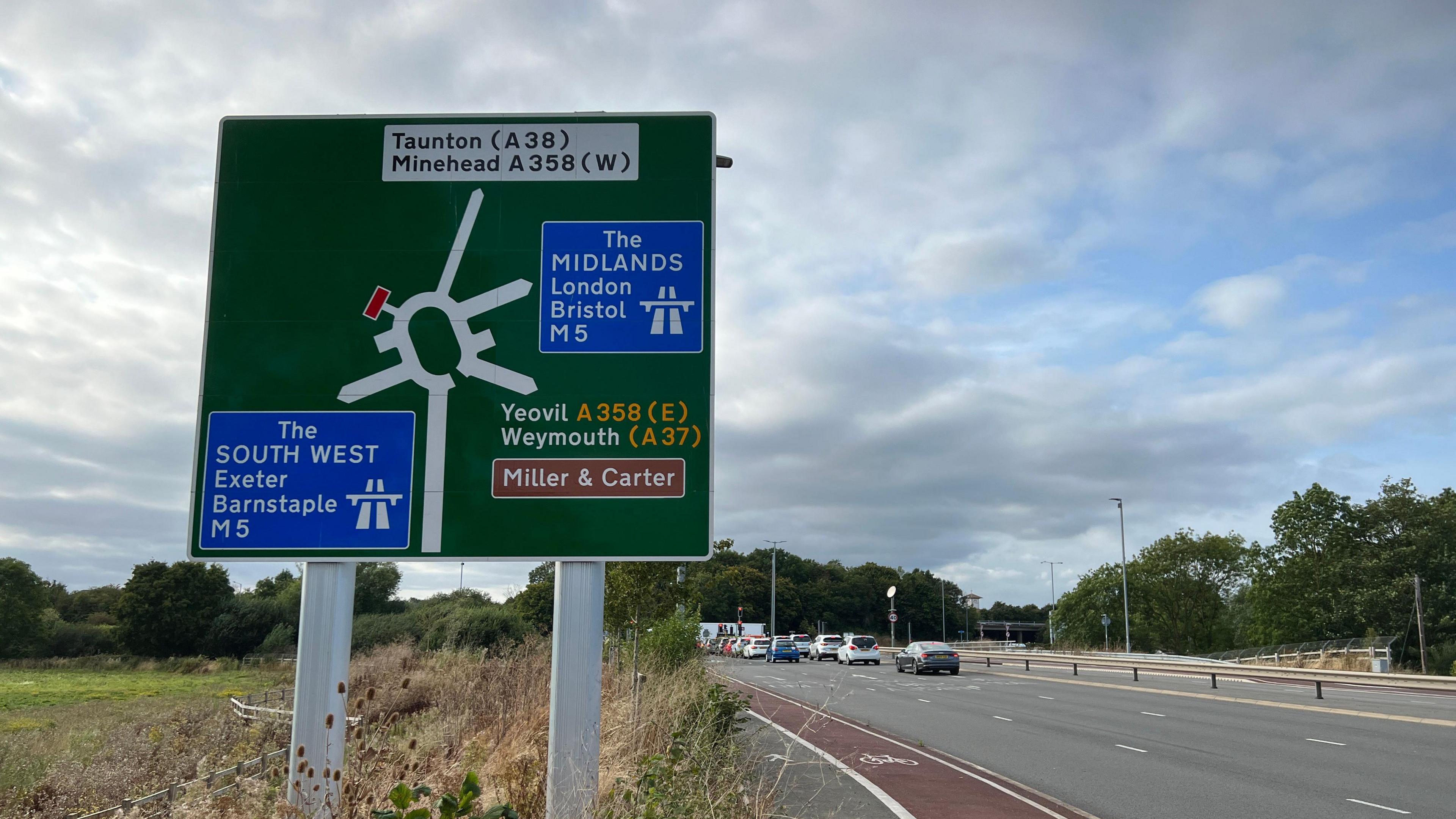 Roundabout sign showing the M5 and A358 roads with a roundabout in the background