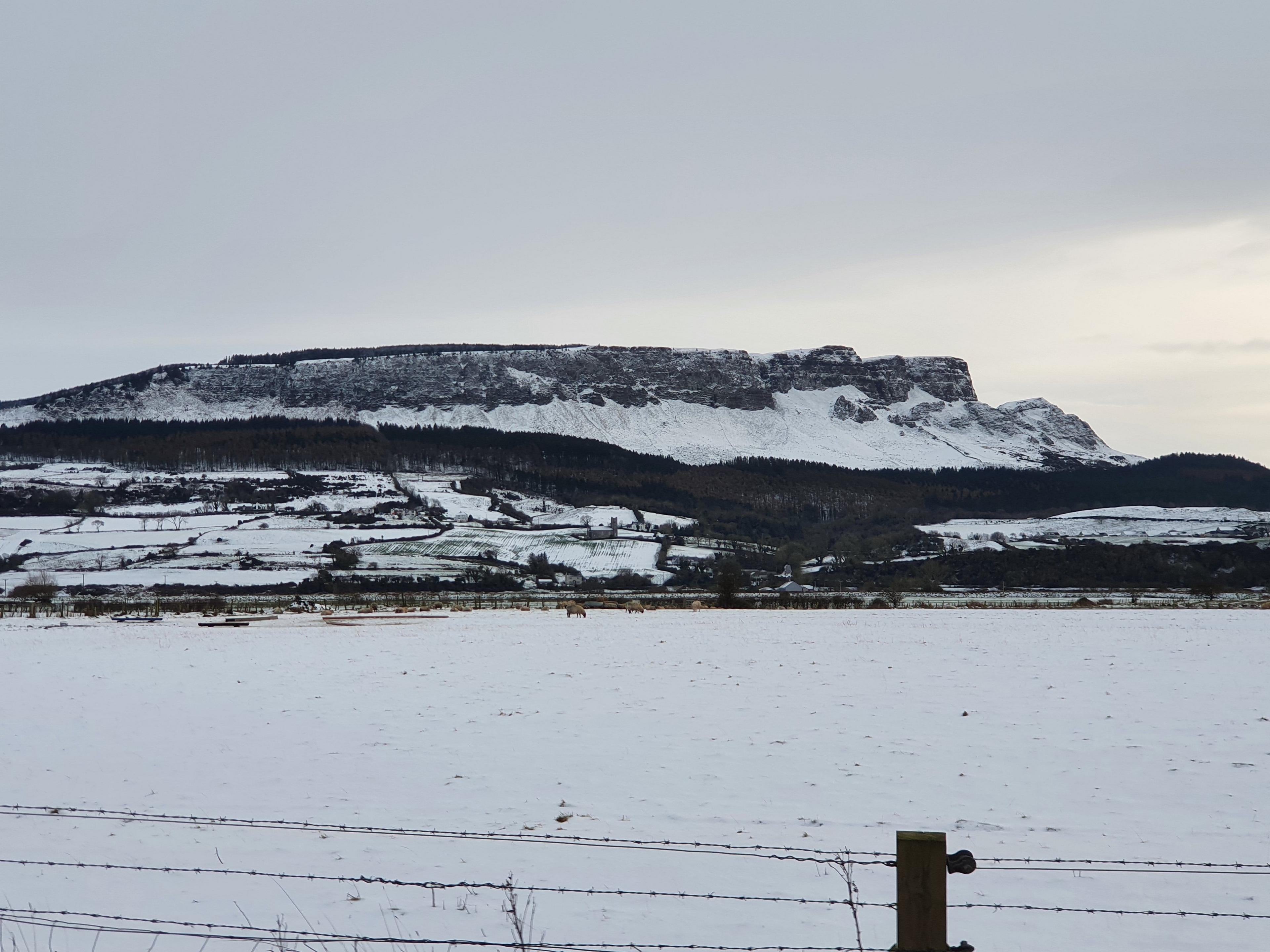 Snow covered Binevenagh, a mountain in county Londonderry, seen from some distance away. A field is in the foreground also covered in snow