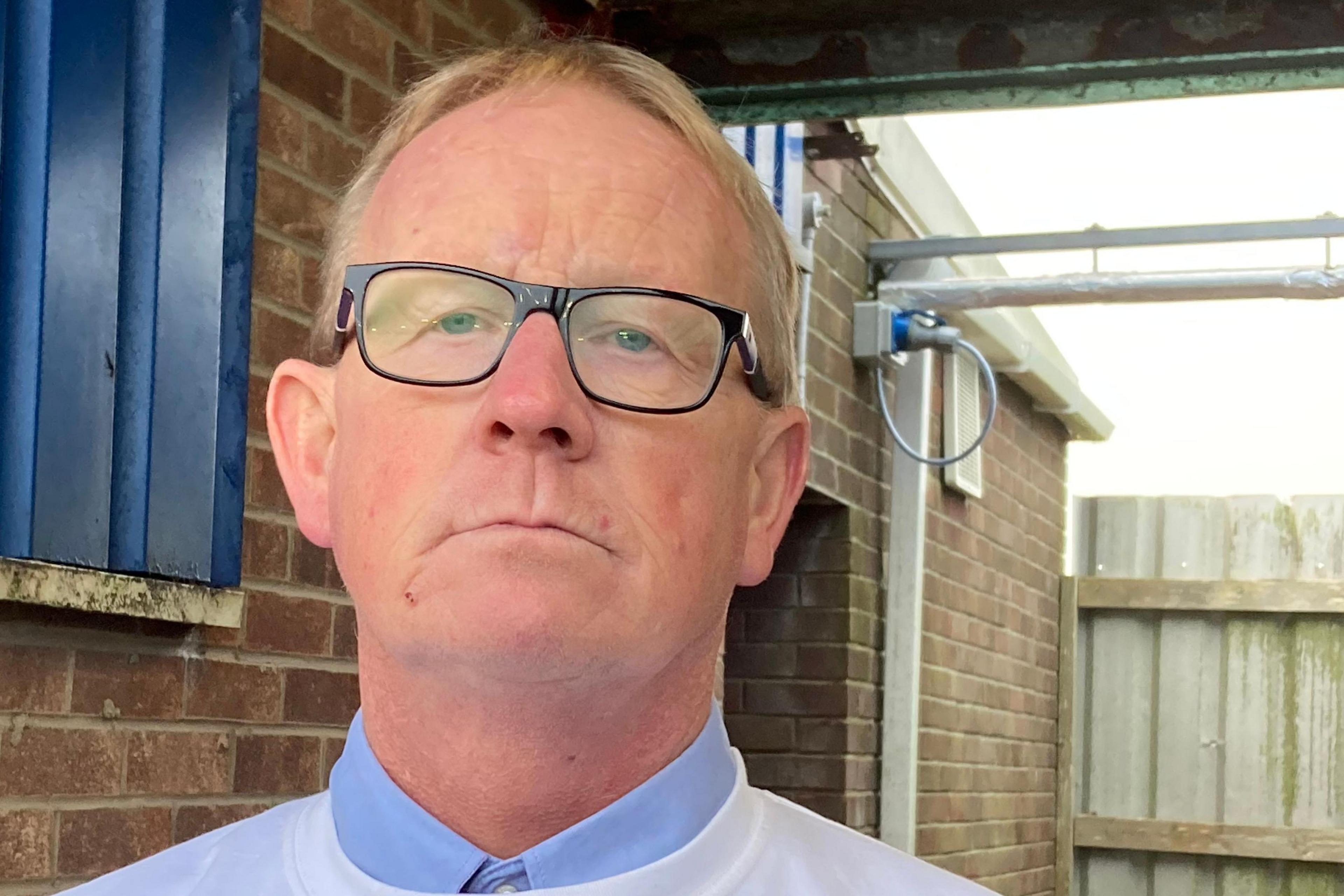 A middle-aged man with fair hair and glasses stands in front of a building at Bridlington Town FC's ground.