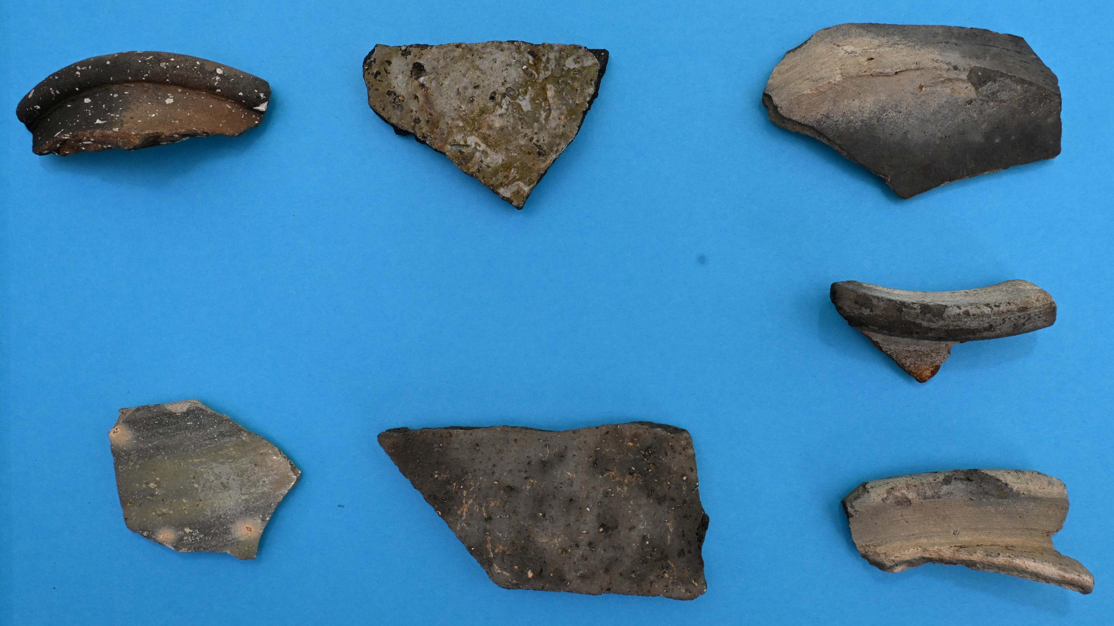 Broken parts of pottery, grey in colour set against a blue background.