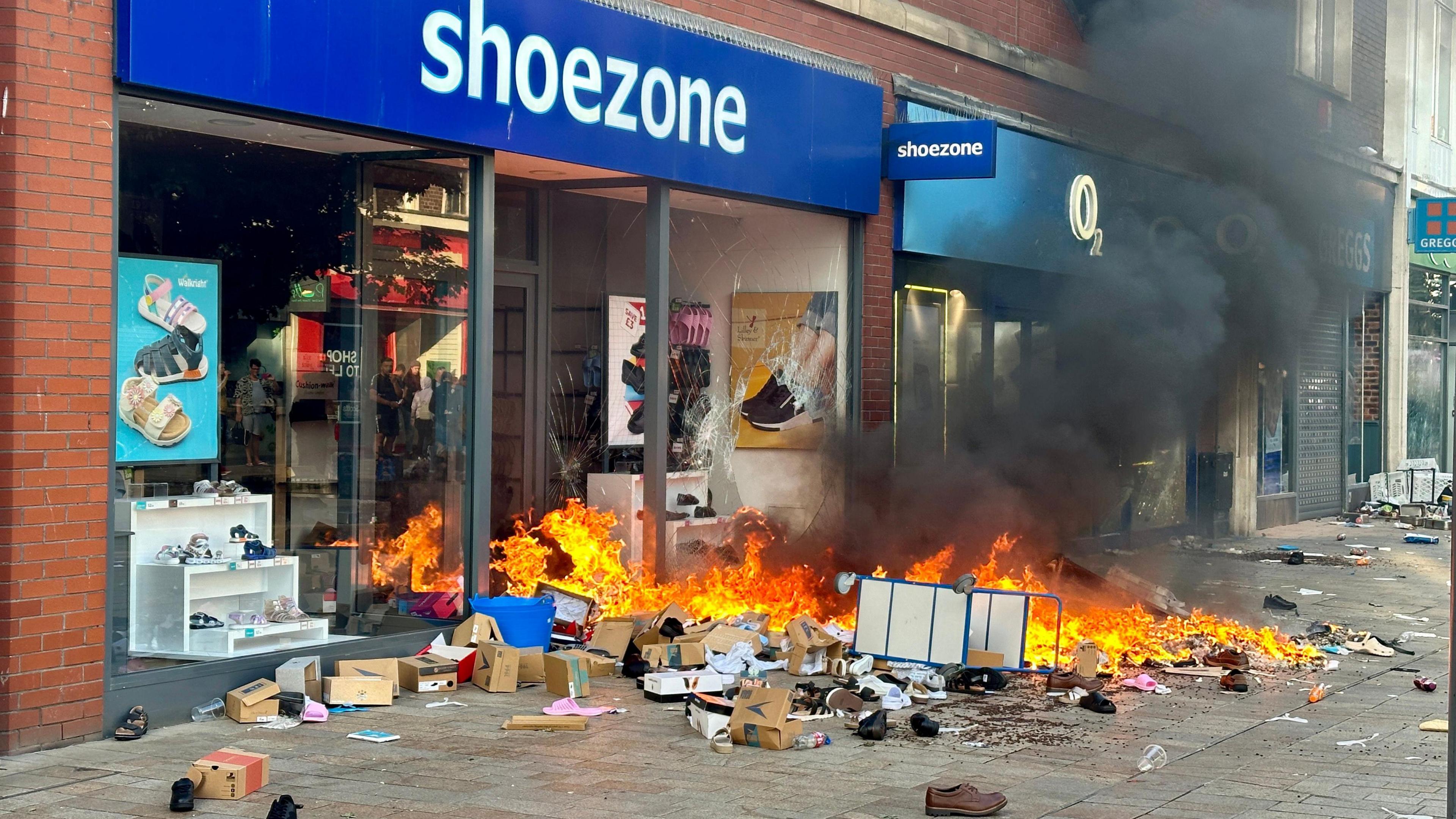 Boxes and shoes are strewn across a pavement in Hull city centre after looting at a Shoezone shop. A window has been badly smashed and a fire rages in the entranceway, creating a plume of black smoke