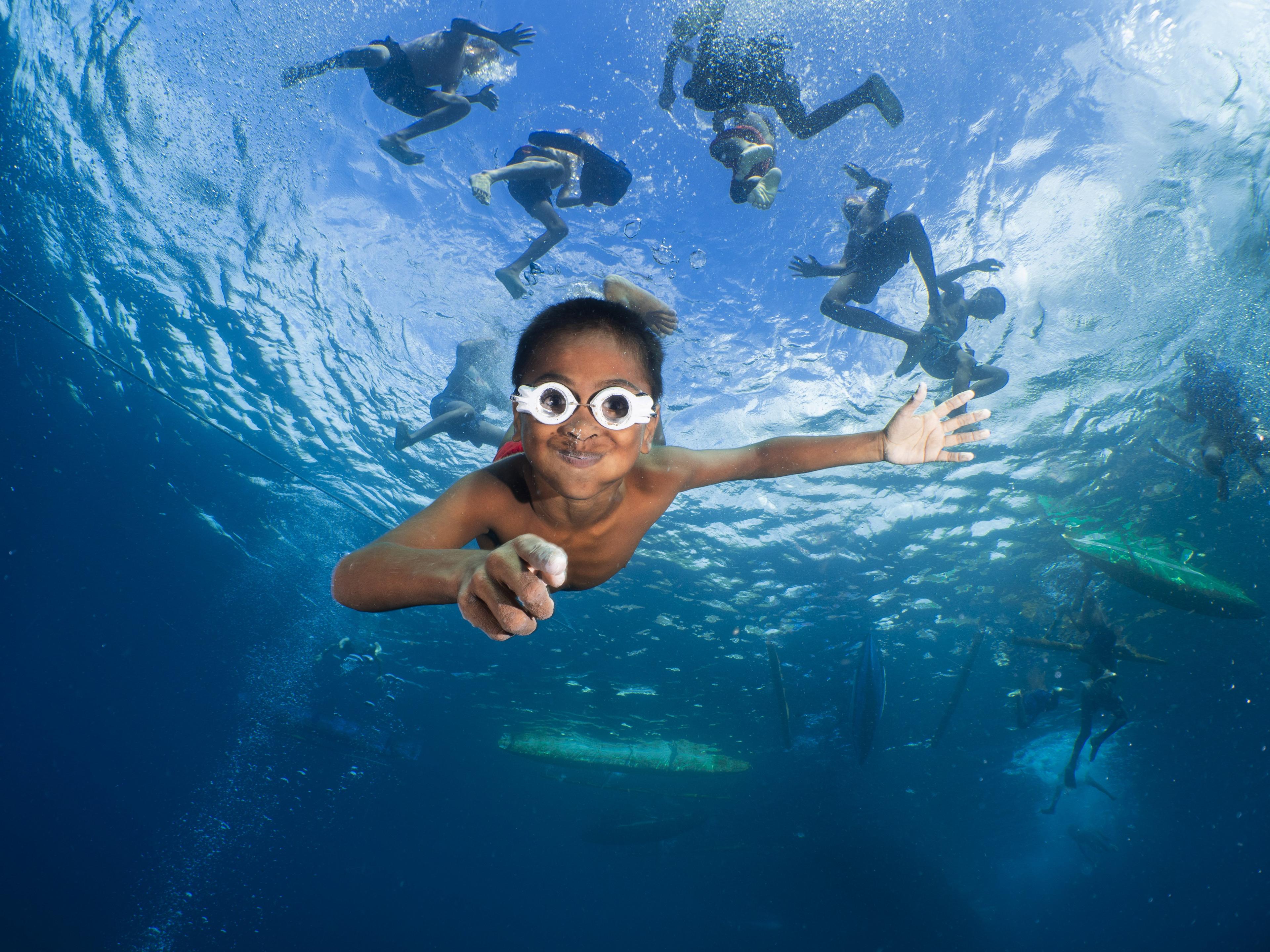 children in Indonesia playing in the water with homemade wooden goggles held together by fishing line.