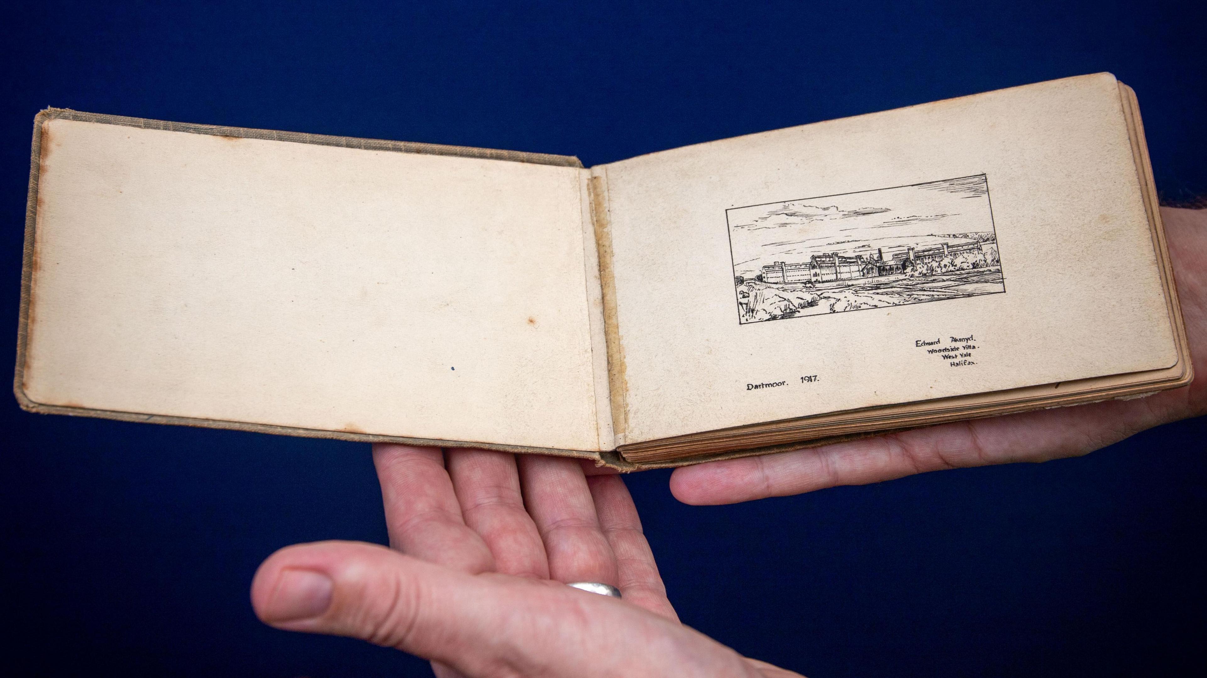 A hand holding the album. It is brown in colour with a image pictured on the right page. The person holding the book is wearing a silver ring. The album looks delicate and is only slightly larger than the person's hand.
