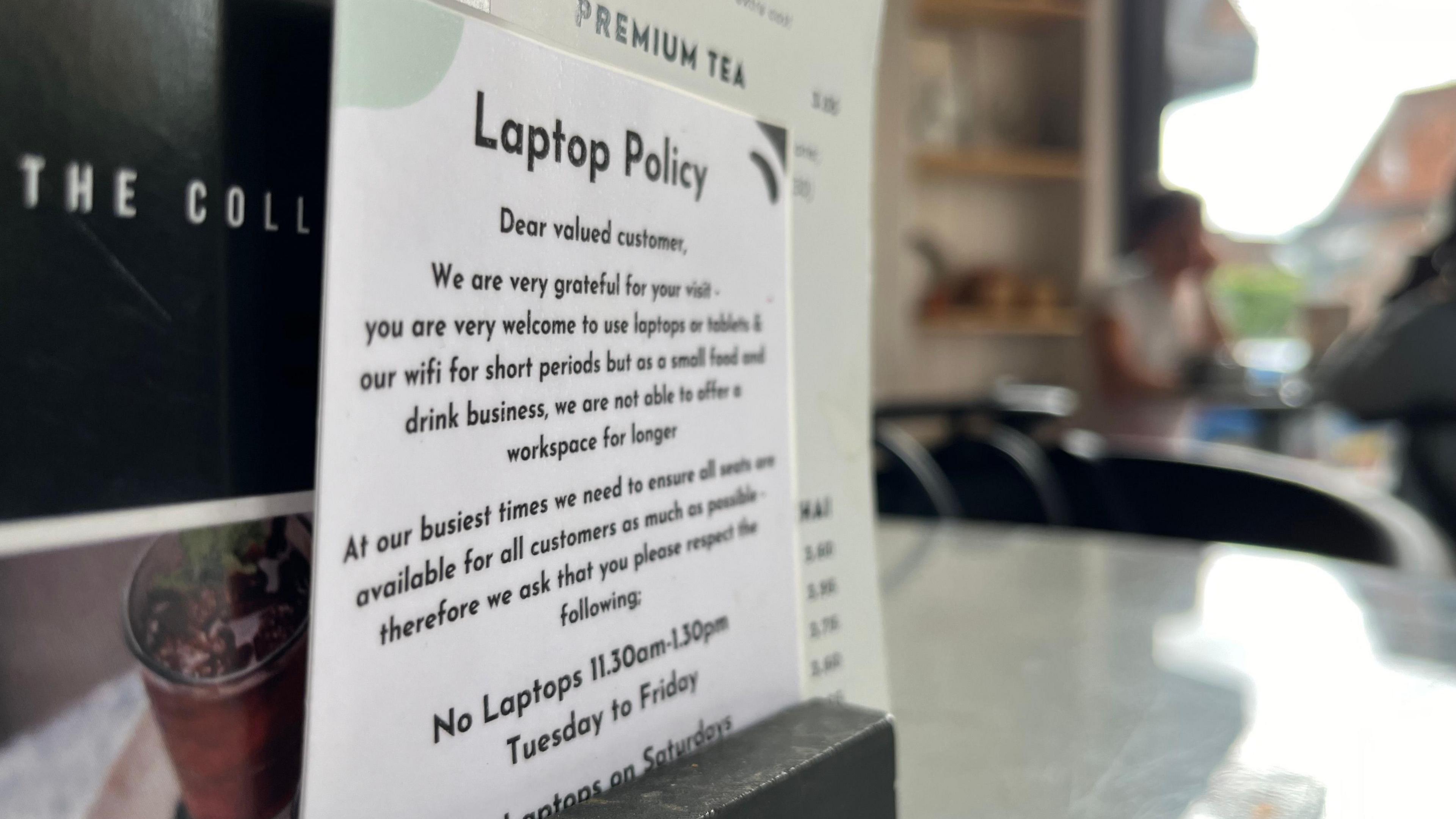 A laminated piece of paper detailing the shops laptop policy, stored with a menu on a table in the shop. The shop itself is out of focus in the background.