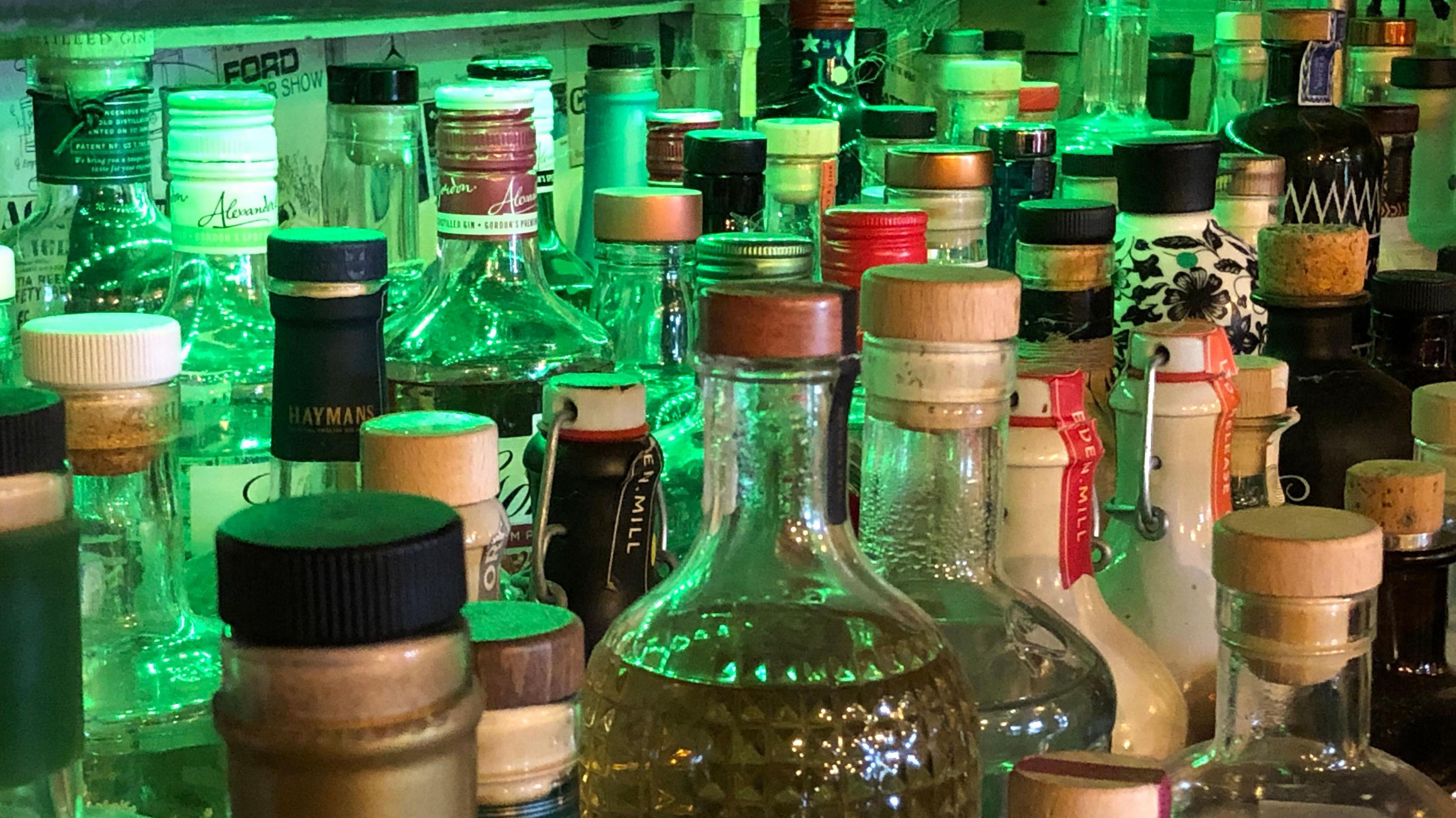 A variety of bottles of spirits on a shelf in a bar, under fluorescent green lighting