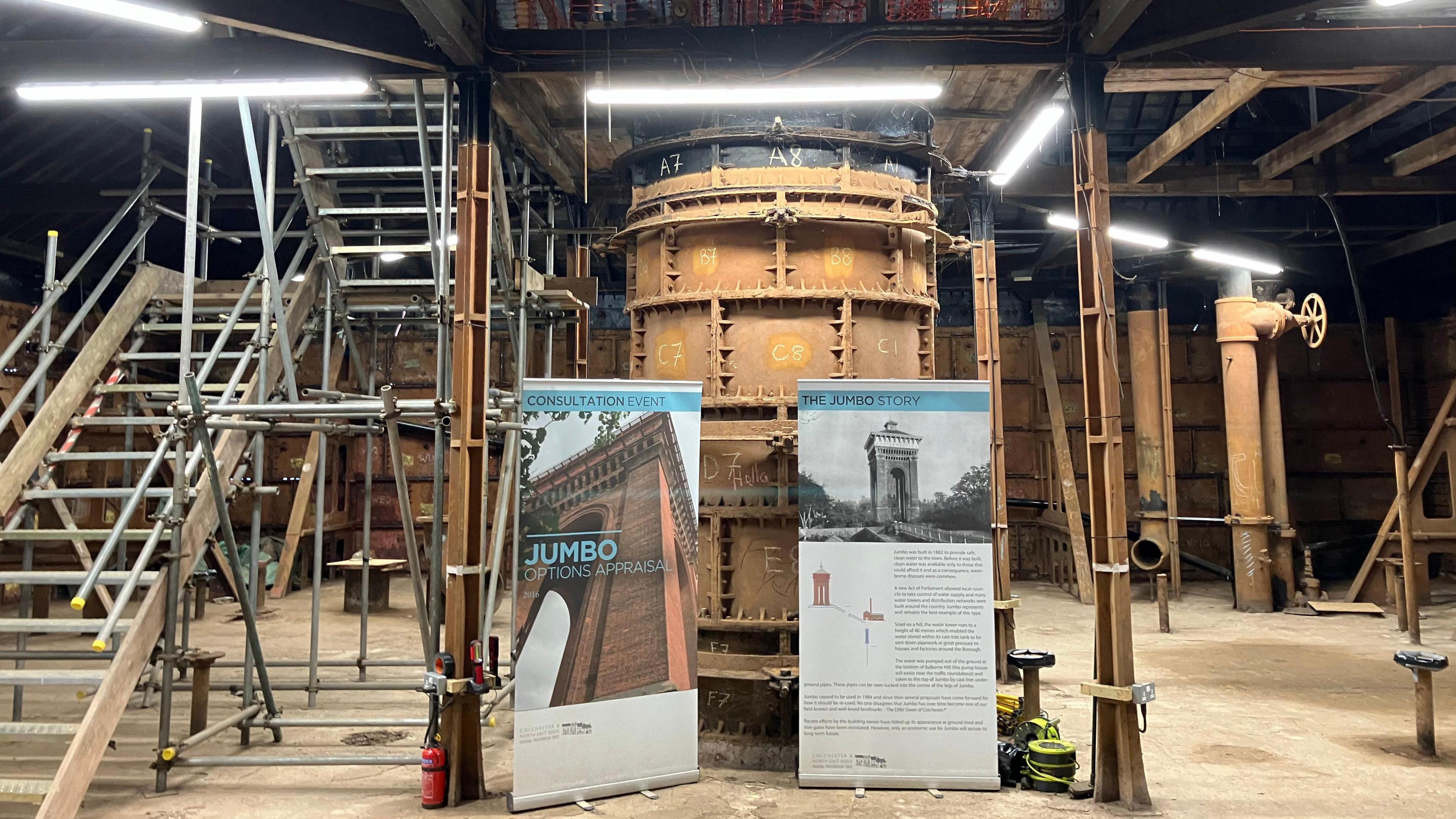 Scaffolding, metal stairs and a large cast-iron pipe are pictured around an industrial-looking room with a very high ceiling