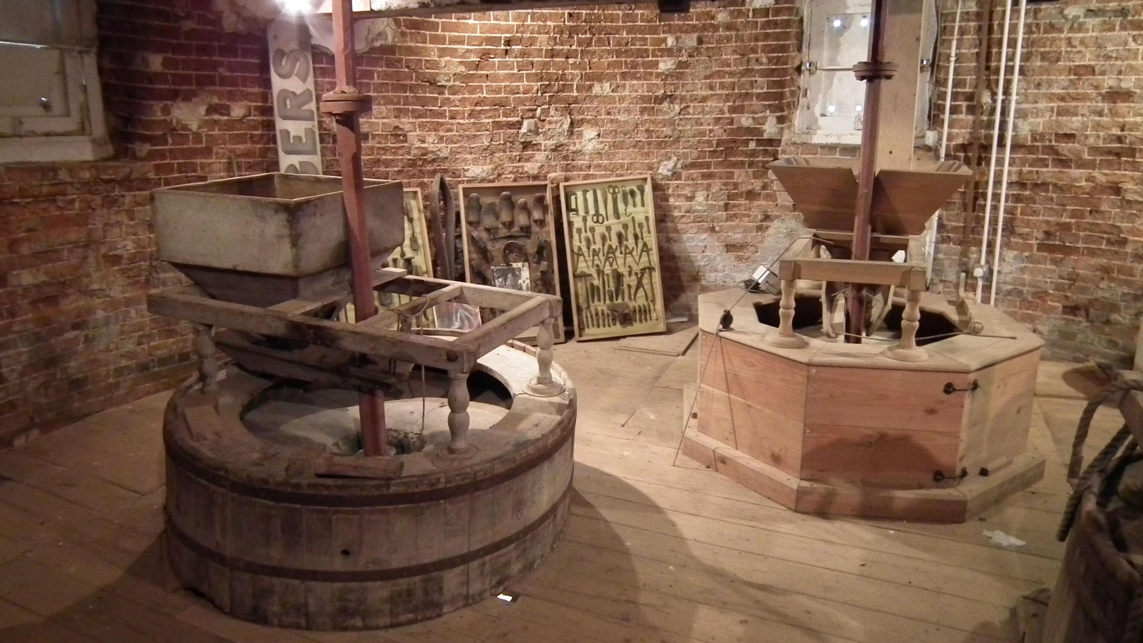 Inside the windmill, which has a brick wall and a wooden floor. There is various milling equipment