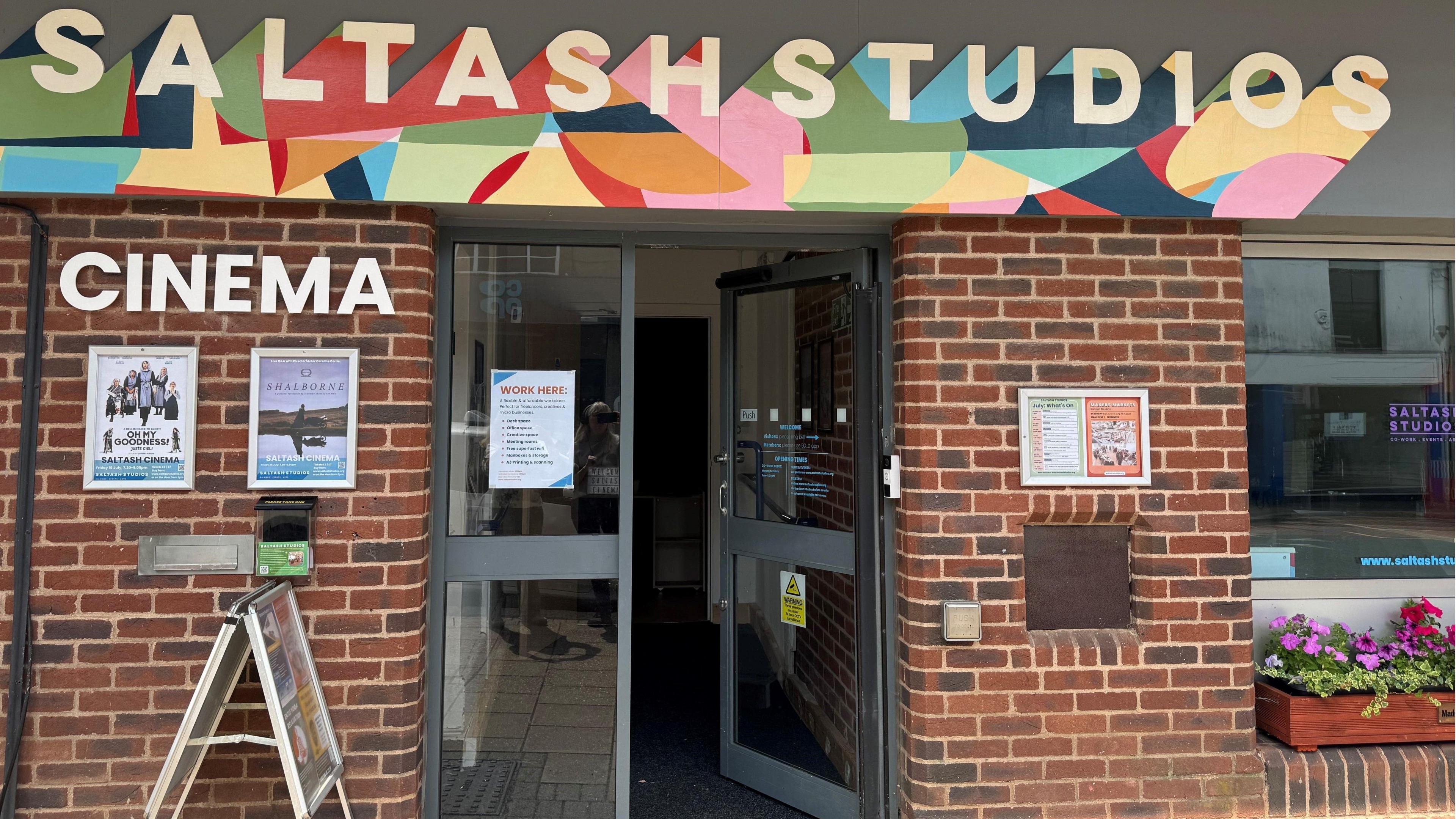 Red brick building with open door and bright and colourful "Saltash Studios" banner and the words Cinema on the side.