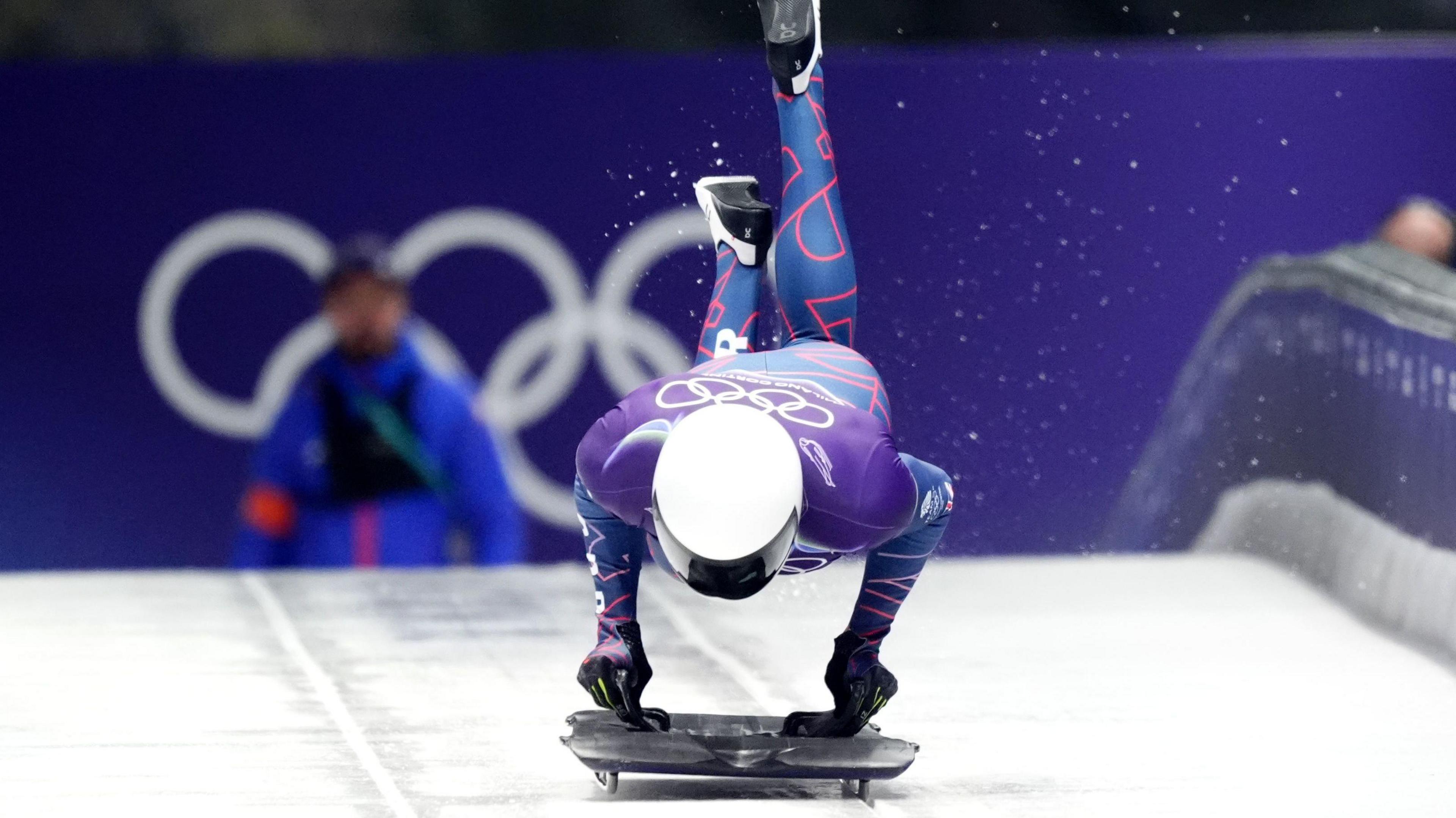 Matt Weston holds his hands on the skeleton slider while his legs are in the air behind him as he jumps onto the slider at the start of a run down the track at the 2026 Winter Olympics