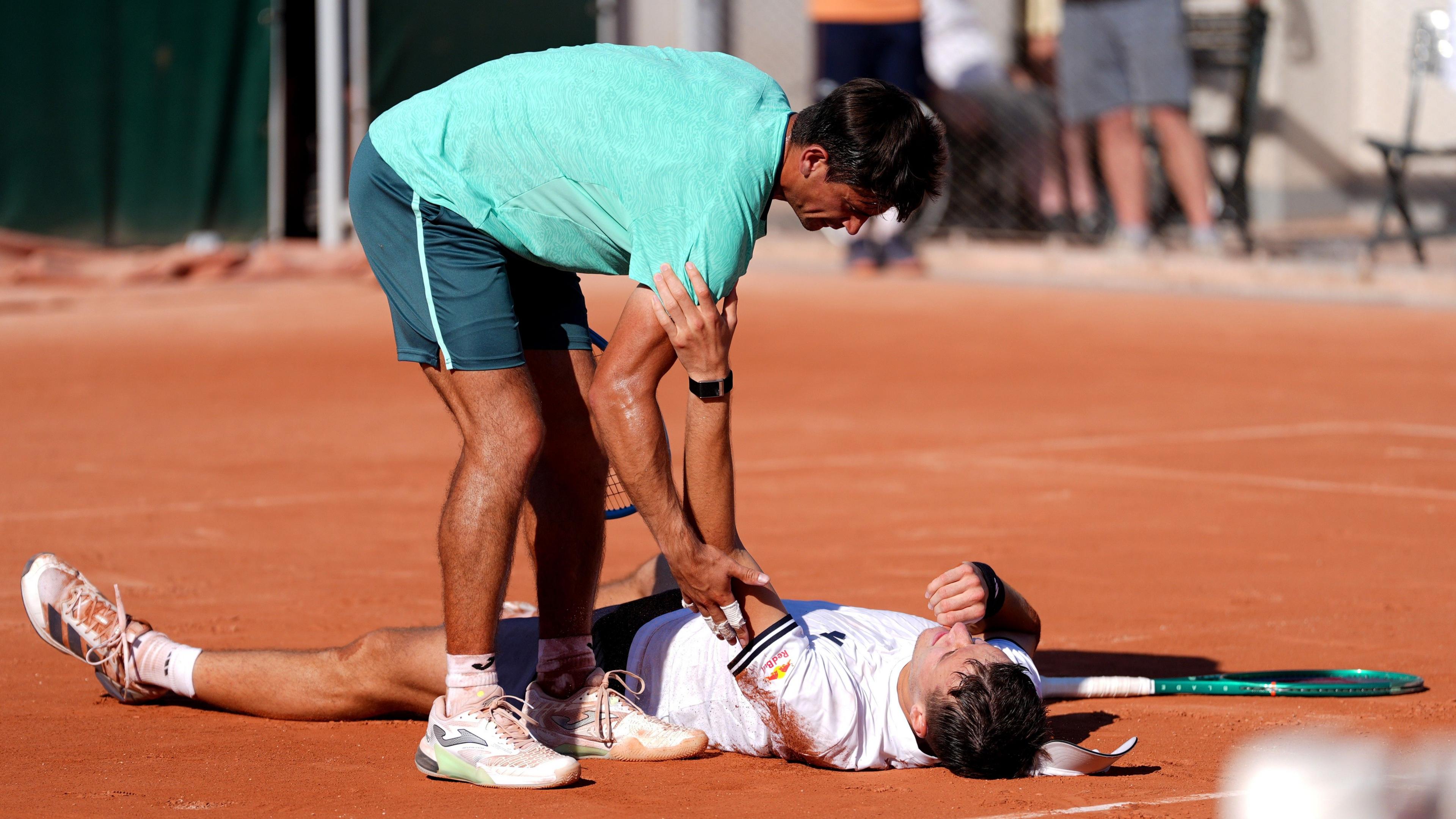 Jakub Mensik lies on the floor and opponent Mariano Navone tries to assist him