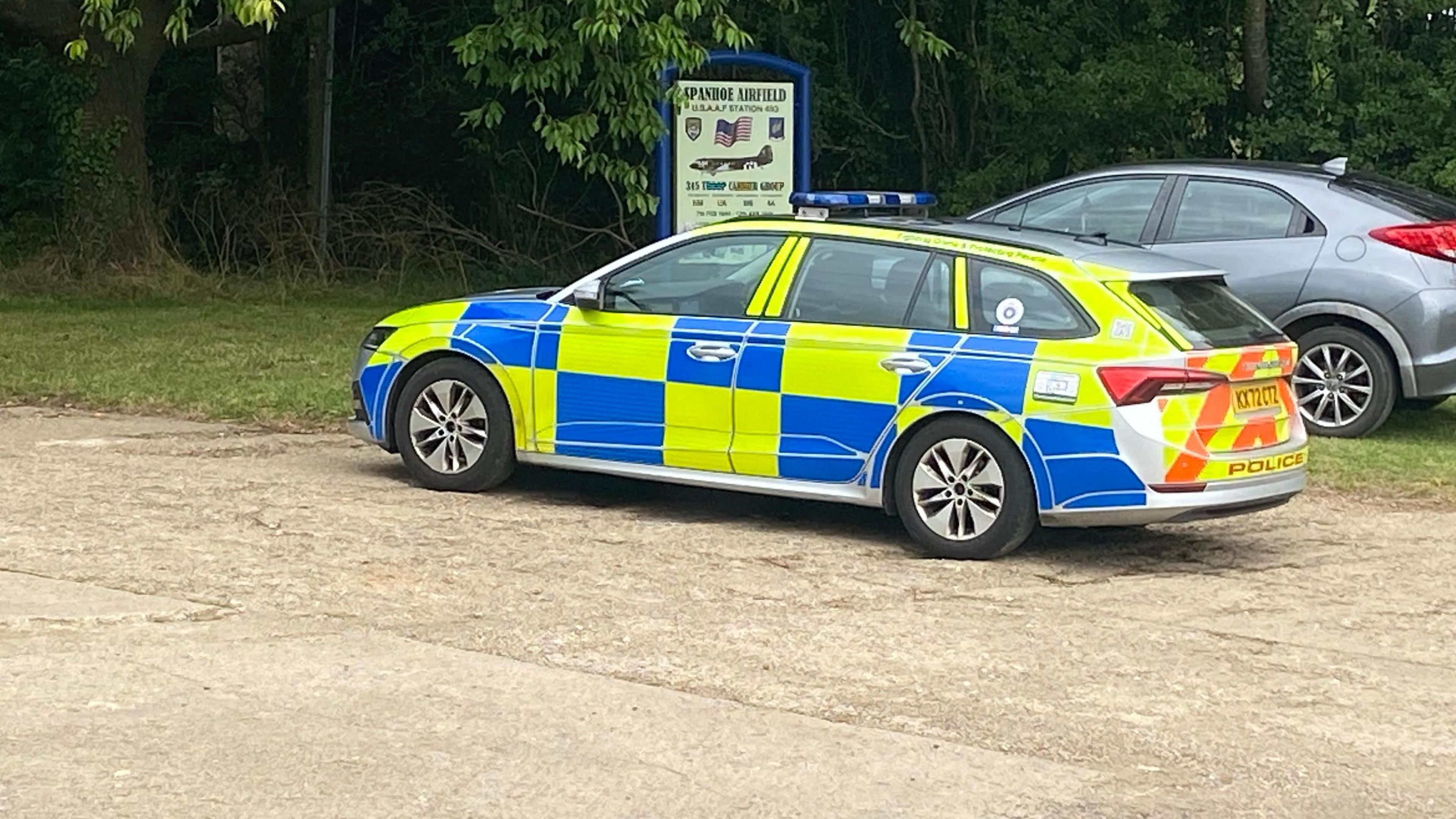 A police car in front of a sign saying Spanhoe Airfield with a silver car behind it