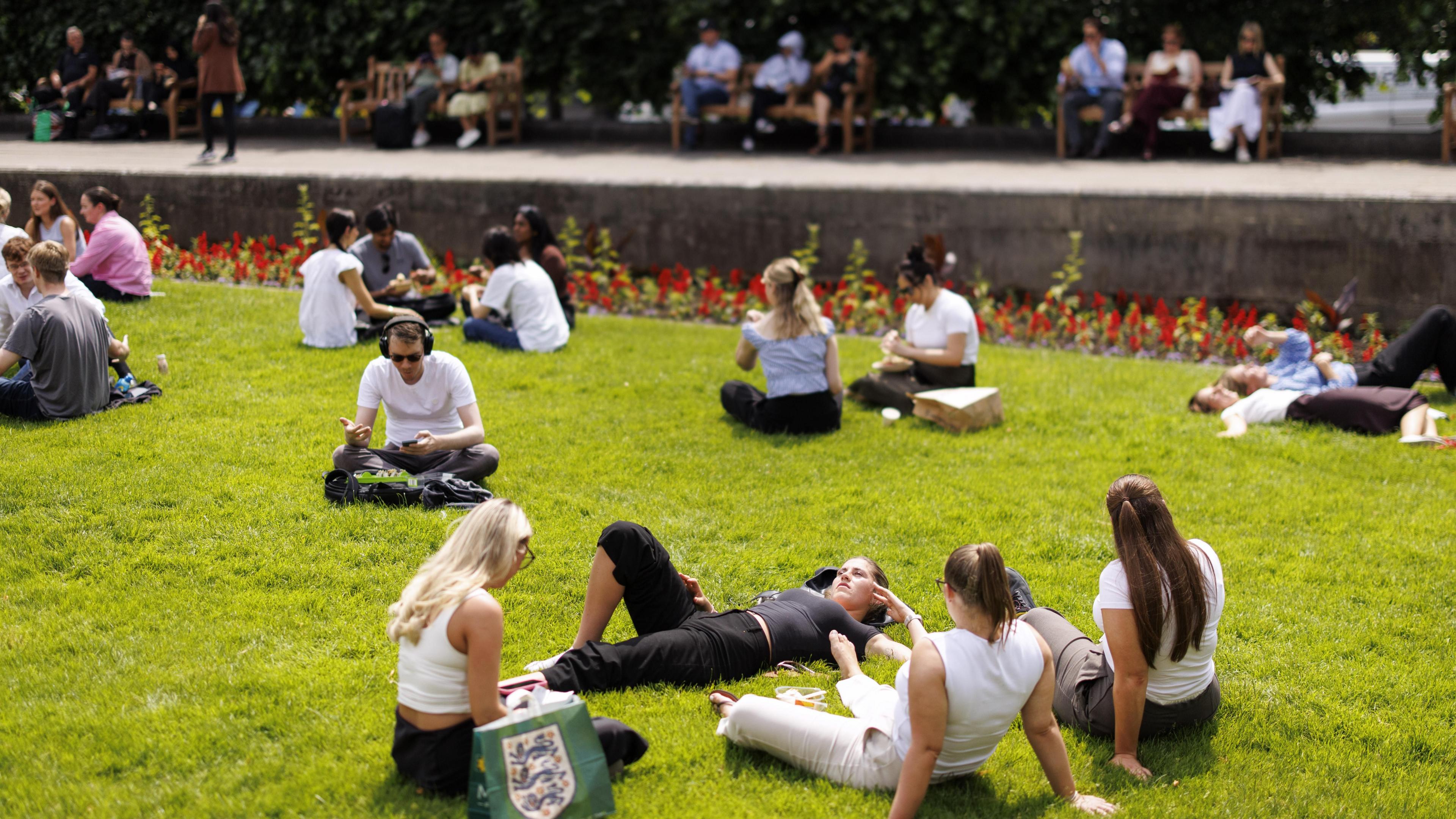 People picnic and enjoy the warm sunshine at St. Paul's Churchyard during lunchtime in the City of London financial district of London.