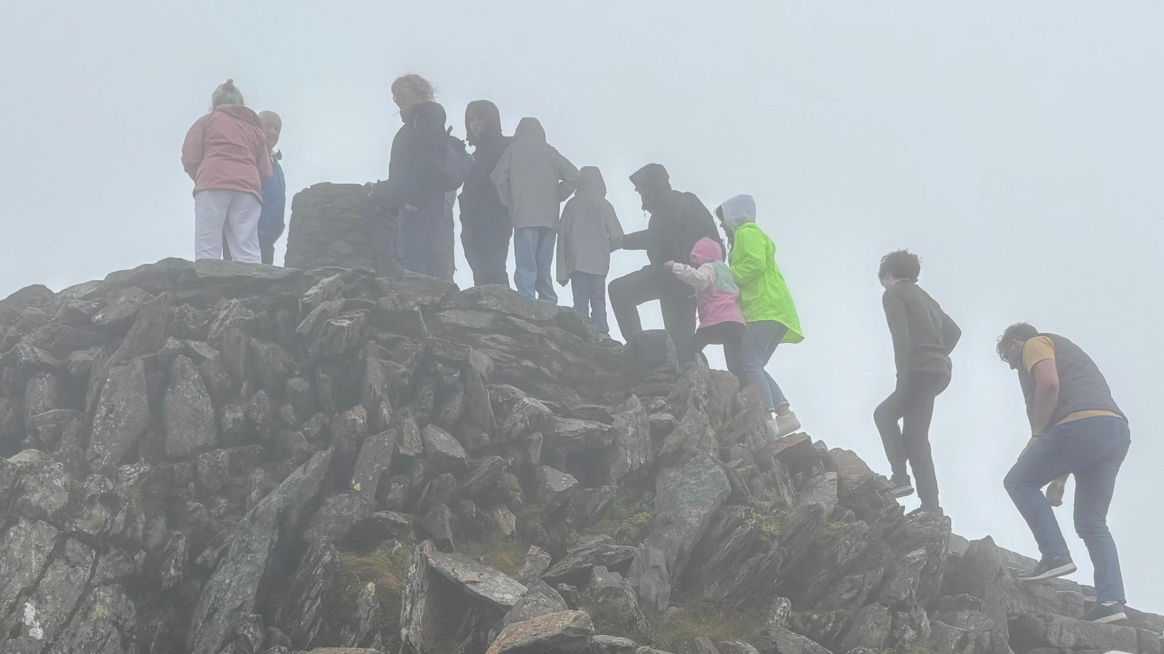 A line of people waiting to reach the trig point at the peak of Yr Wyddfa on a misty day