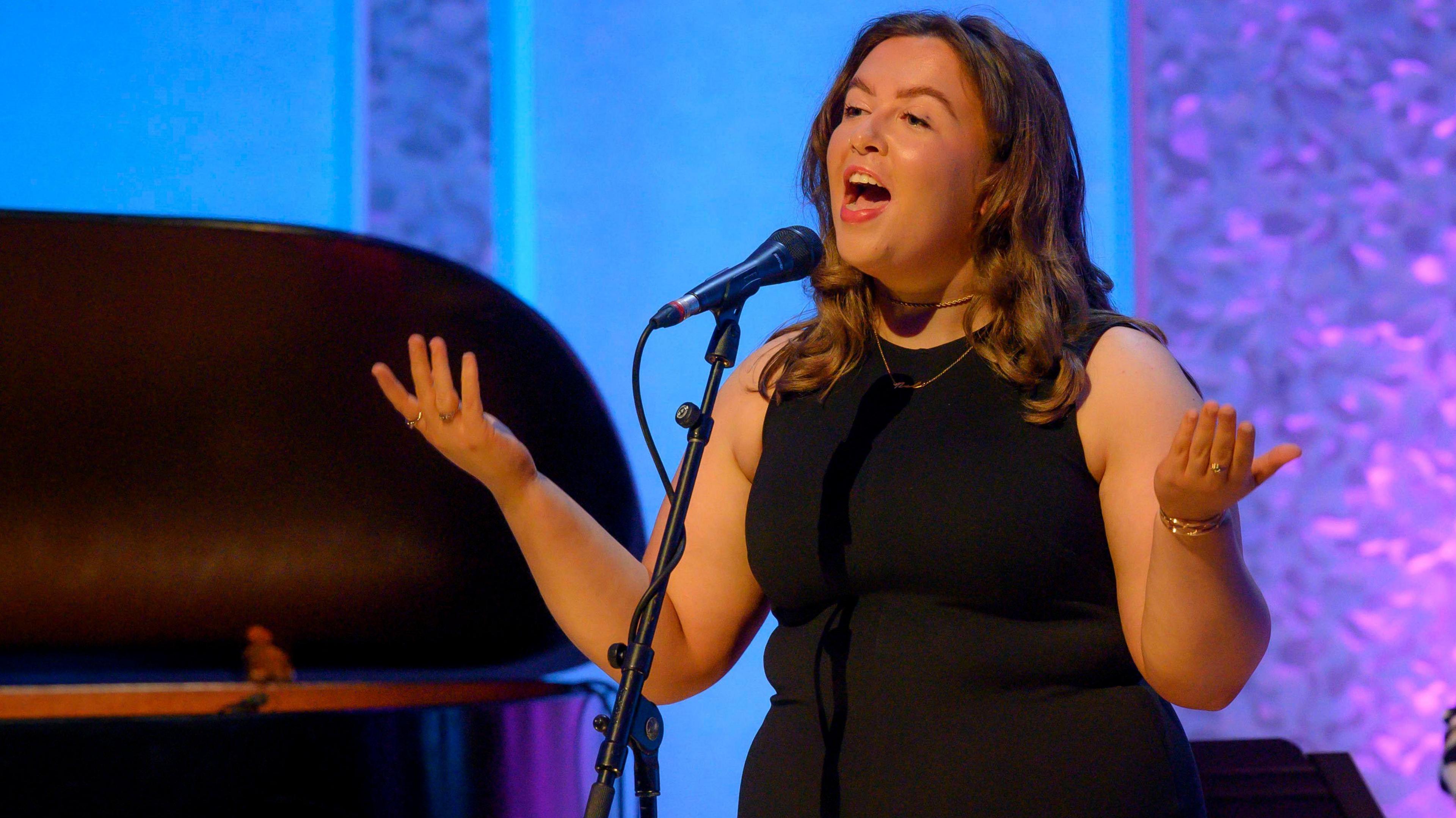 Ellie Beaton signing on stage at the awards ceremony, wearing a long black dress