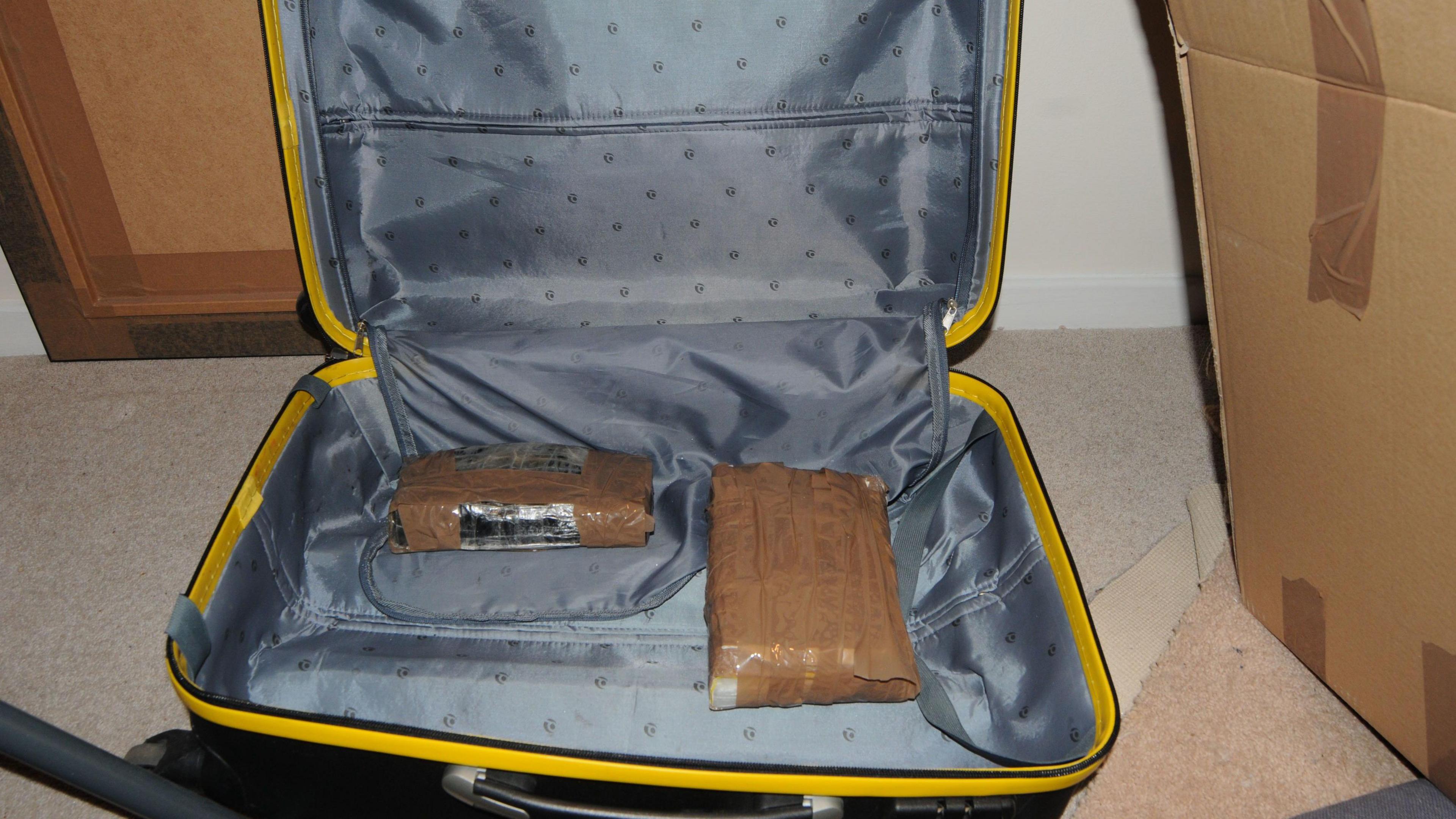 A black suitcase with a yellow trim, open to reveal two brown packages taped over.