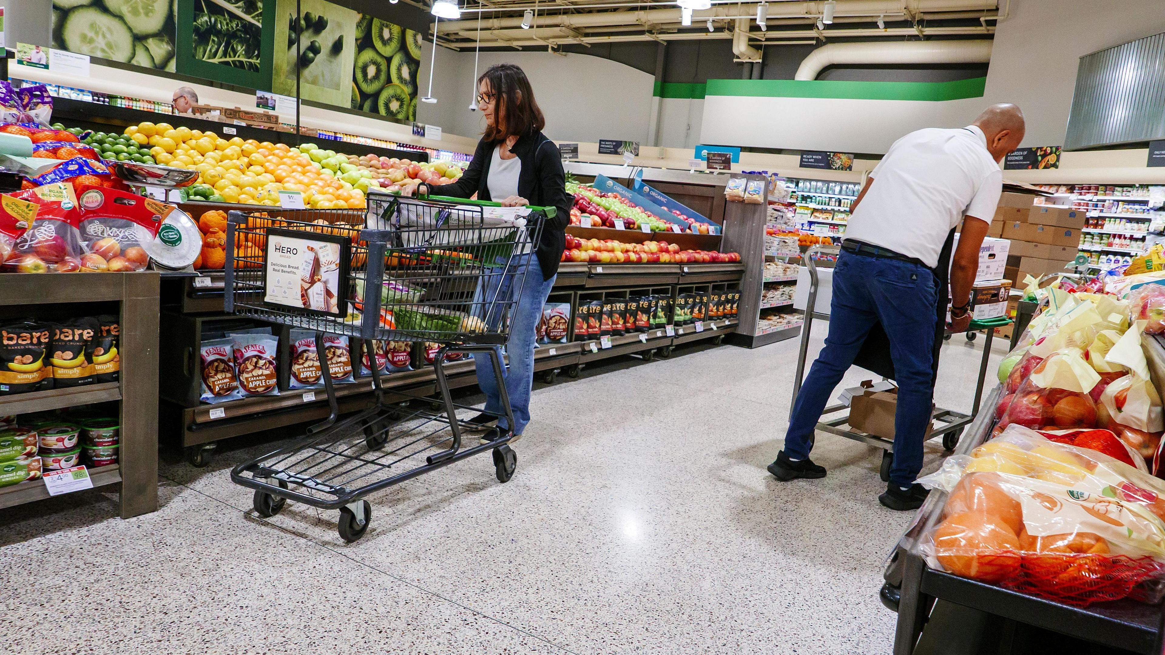 A woman pushes a grocery cart while shopping for groceries at a supermarket.