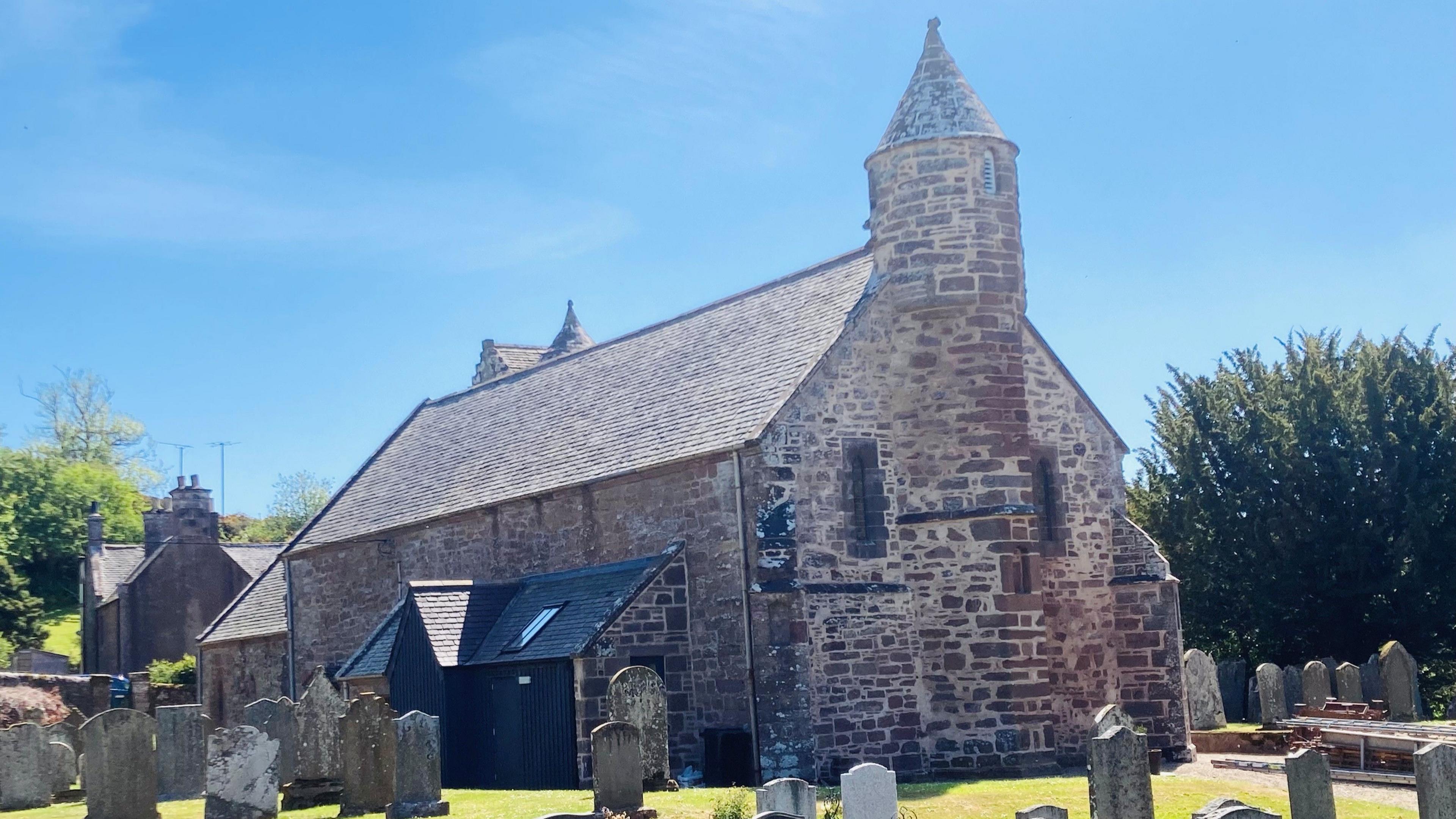 Church building - Arbuthnott Church - with graves in the foreground, under a blue sky.