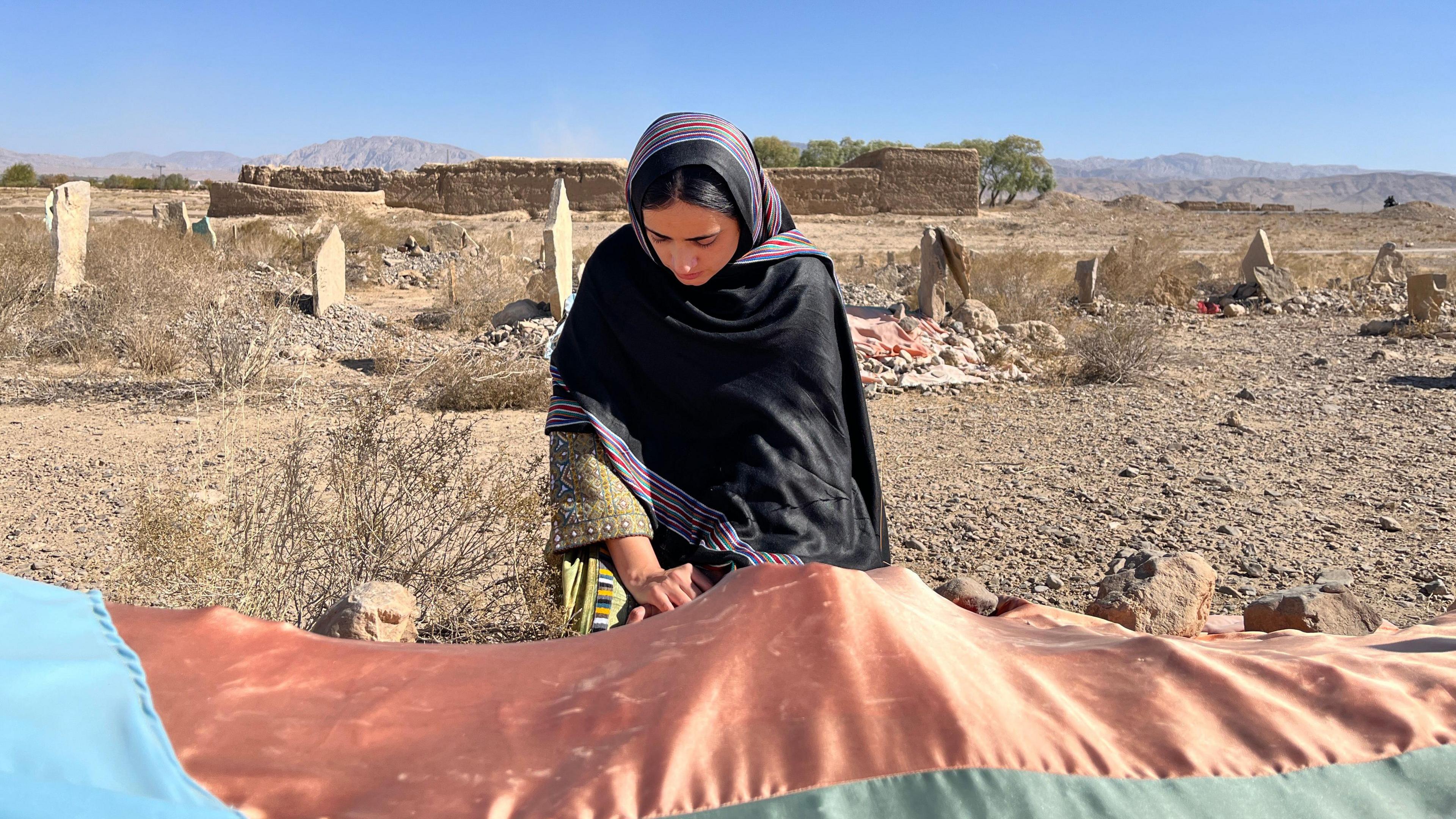 Mahrang kneels at her father's grave in a black shawl