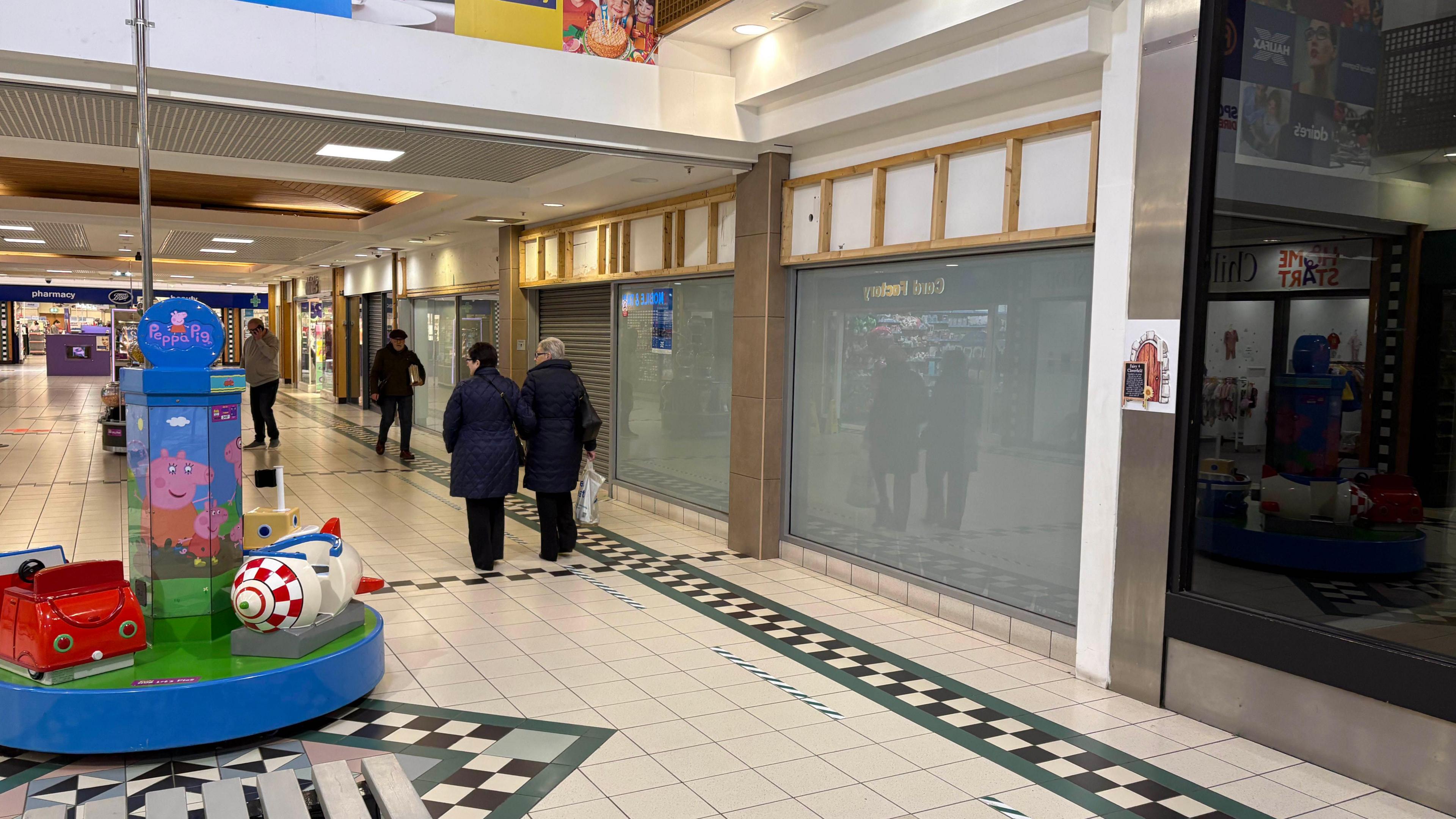 Inside of Connswater Shopping Centre, showing floor tiles and windows - empty units are seen with shoppers walking past them