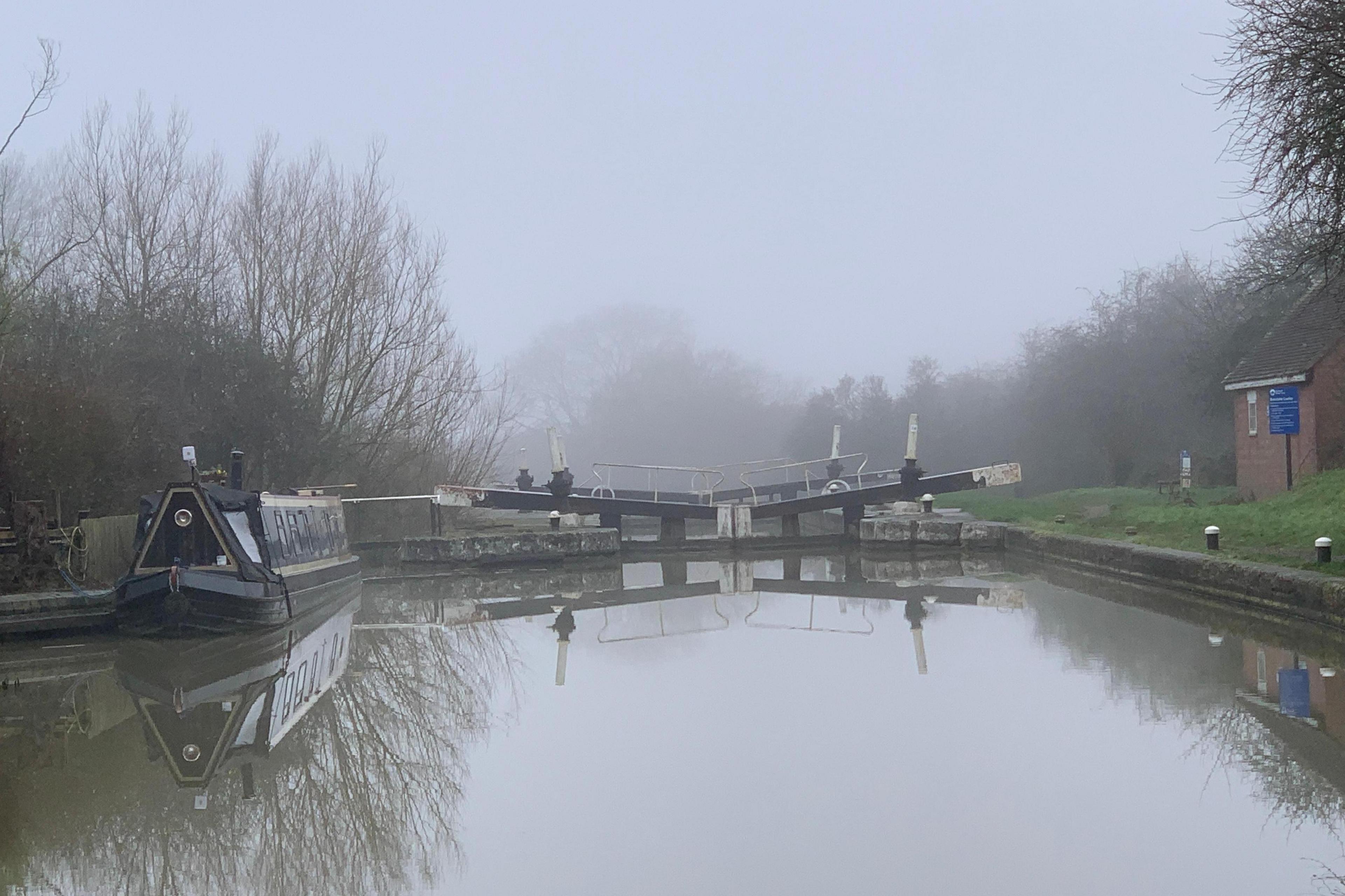 A misty canal lock in Warwickshire. A narrowboat is moored up on the left, with the locks in the centre and grass on the right bank.