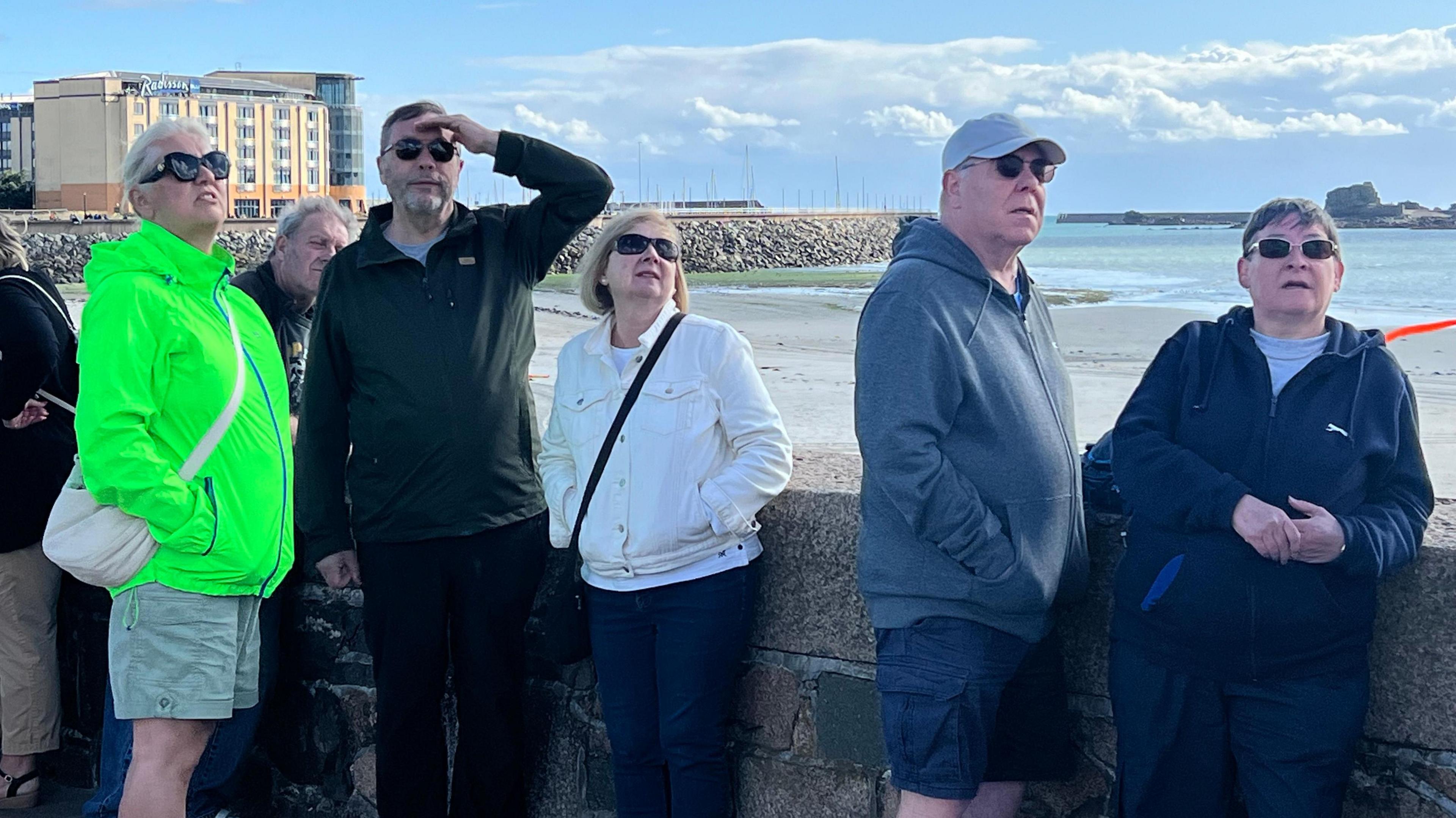 A group of six people standing on the waterfront and looking to the skies during a display at the Jersey International Air Display