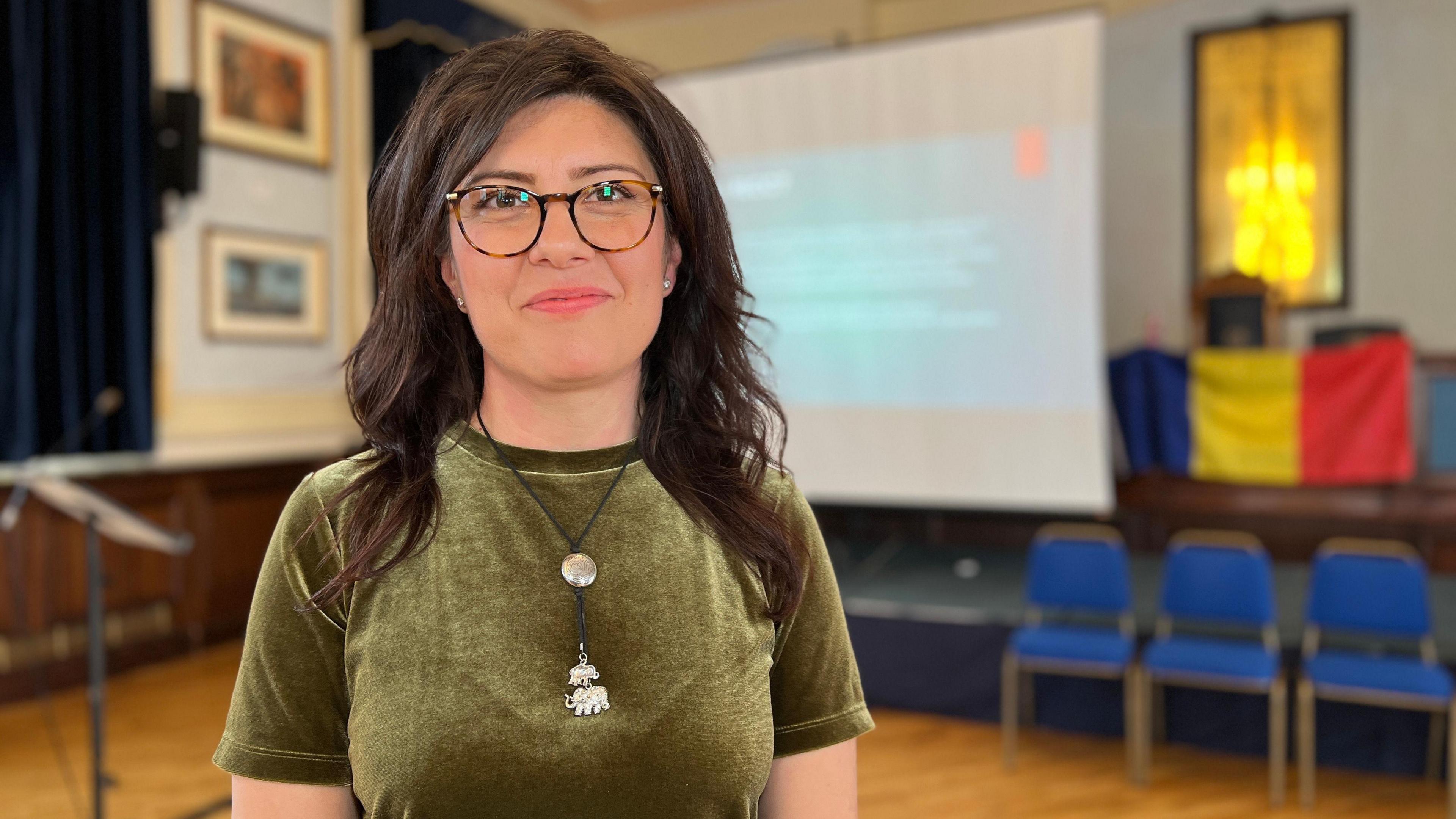 Corina smiles at the camera and behind her is a projector screen with details of the course on it with a Romanian flag to the side