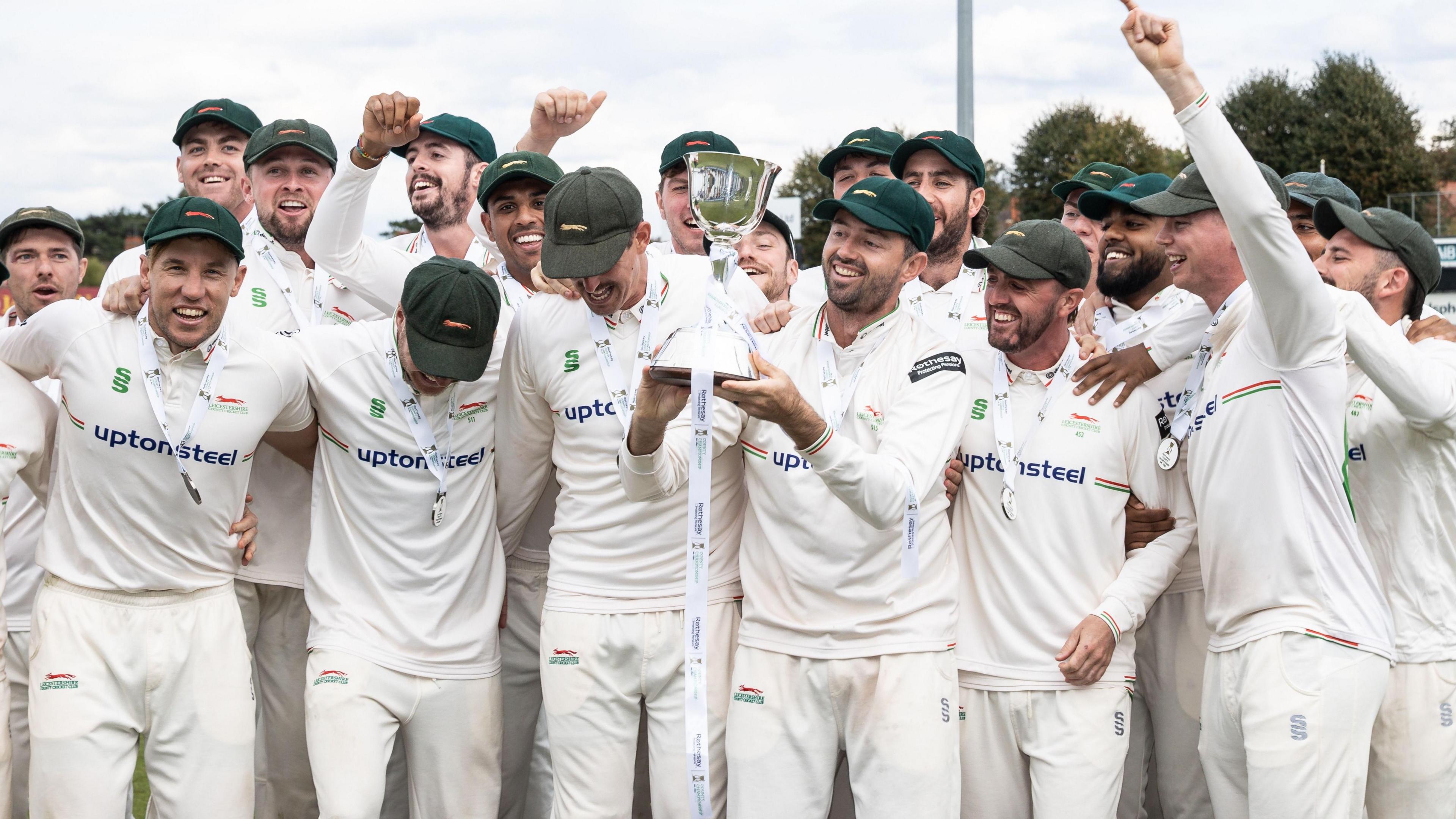 Leicestershire players celebrate in a large group together as Ian Holland lifts the trophy aloft in the centre to after winning promotion from Division Two
