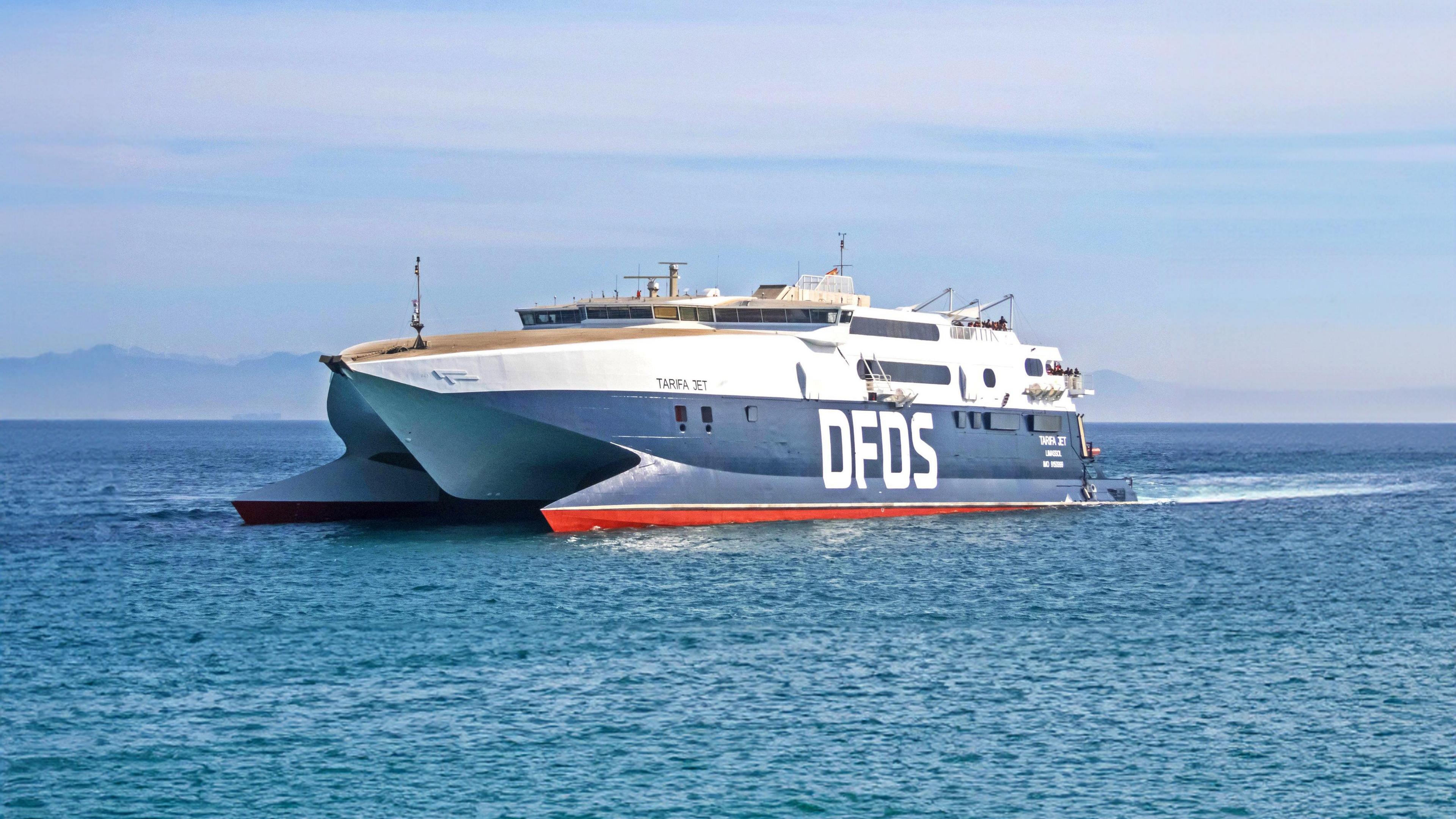 A blue and white vessel with DFDS branding and the name Tairfa Jet on the side sailing across a blue sea.