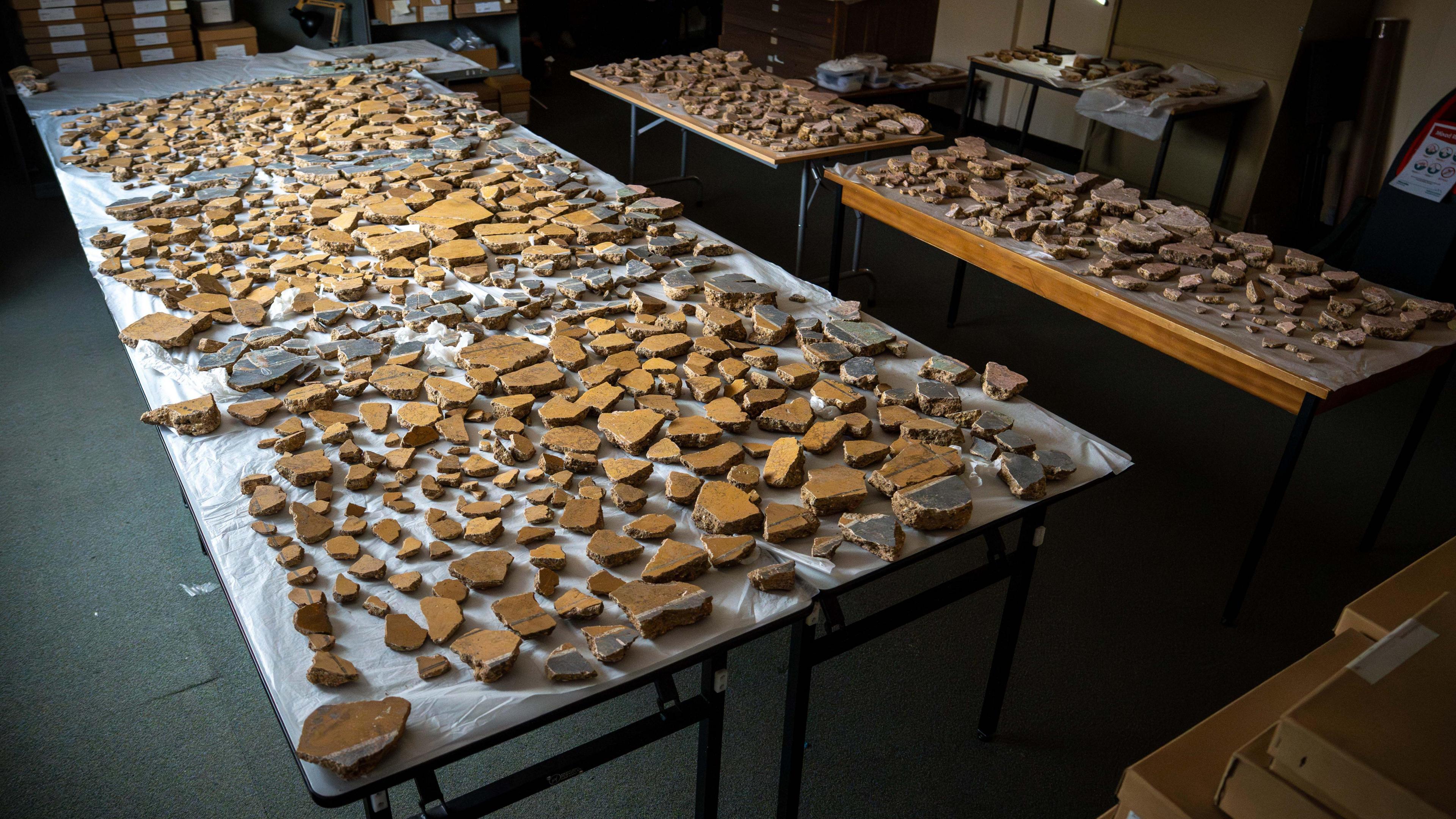 Hundreds of fragments of plaster laid out on several tables. Mainly yellow pieces making up three square panels with darker columns in between.