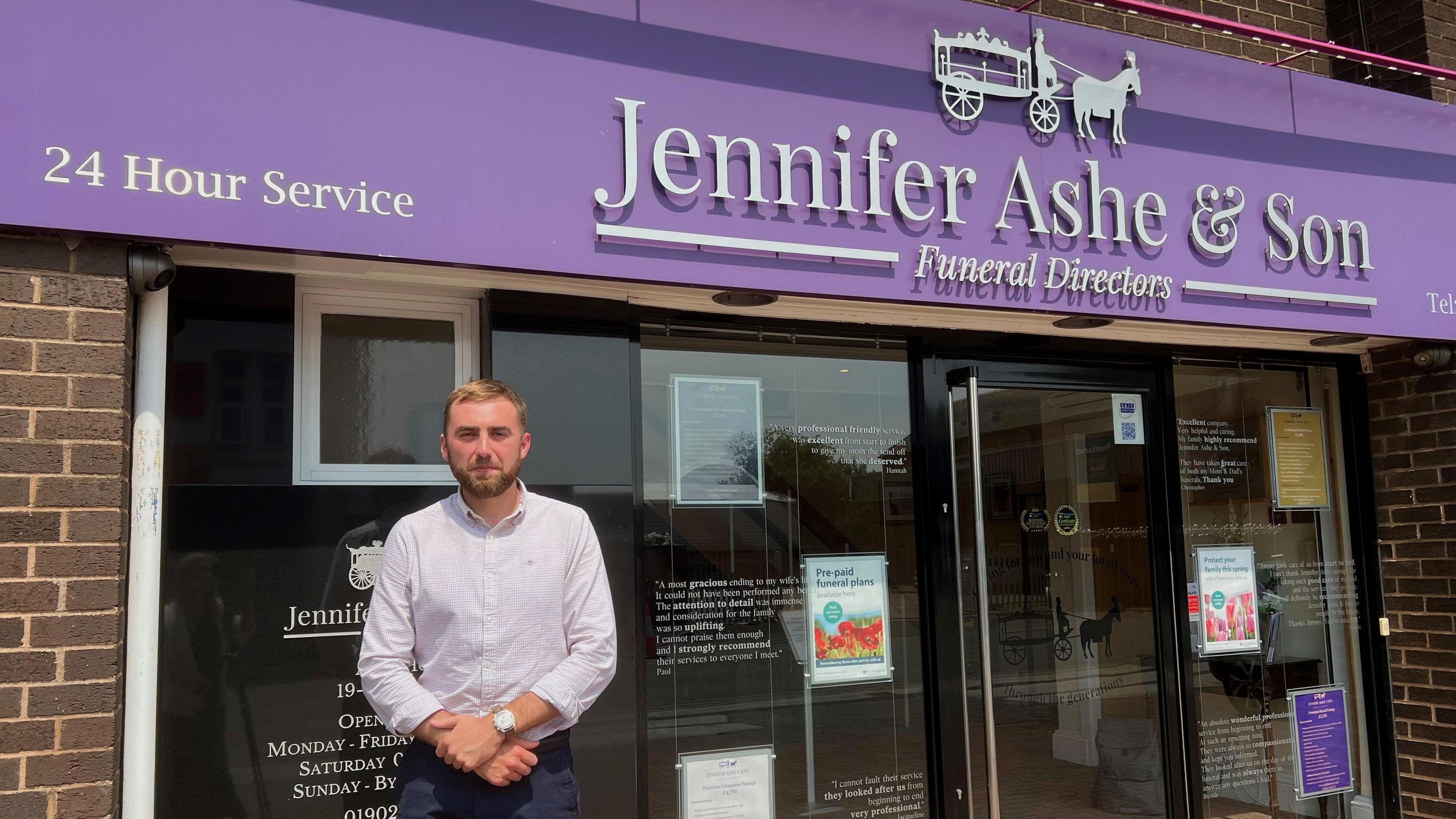 A man standing in front of a purple funeral directors sign