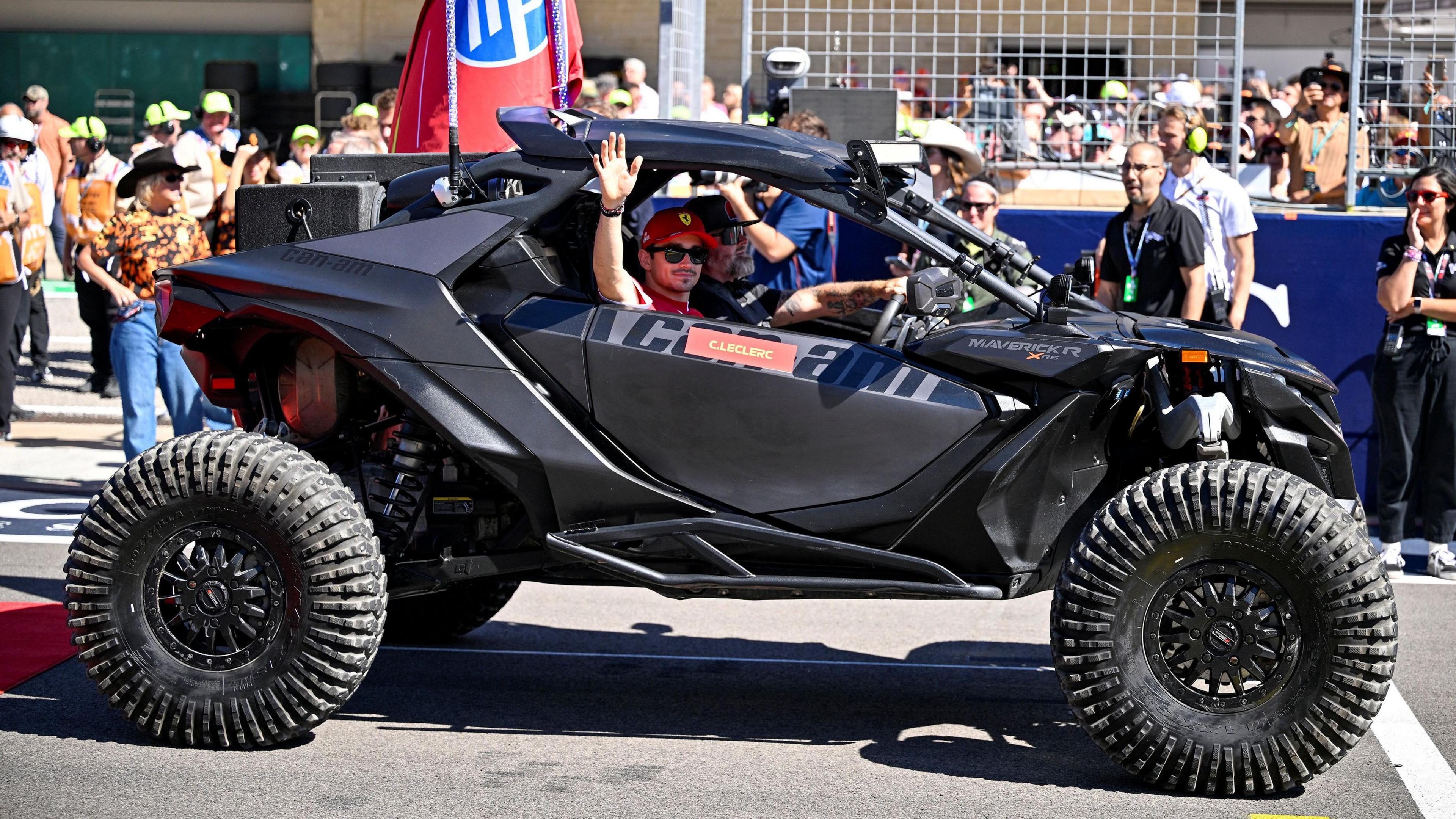 Charles Leclerc waves to fans from a black off-road vehicle during the drivers’ parade