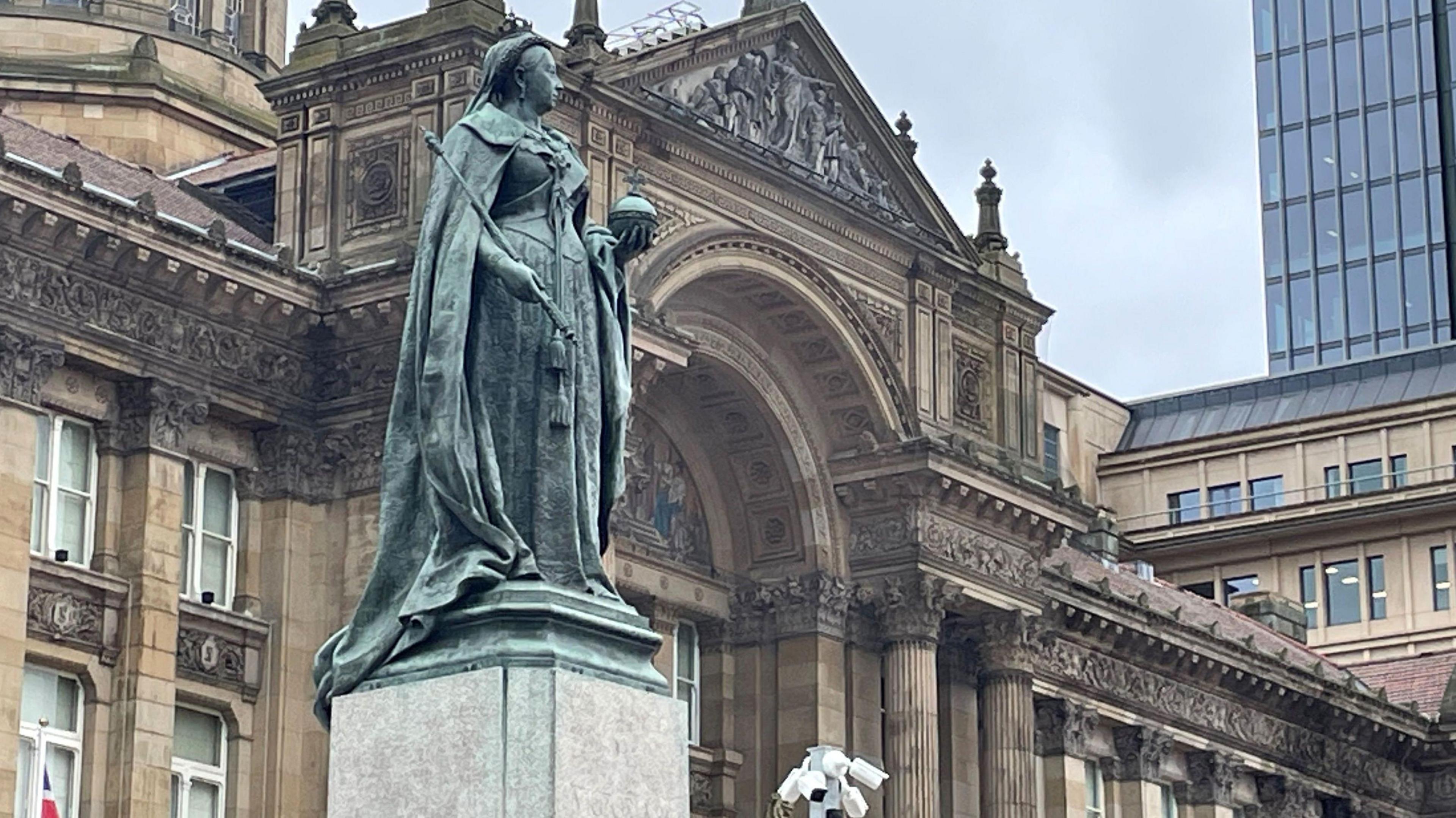 A green metallic statue of Queen Victoria at the front of Birmingham Town Hall, a stone building dating back to the 1830s.