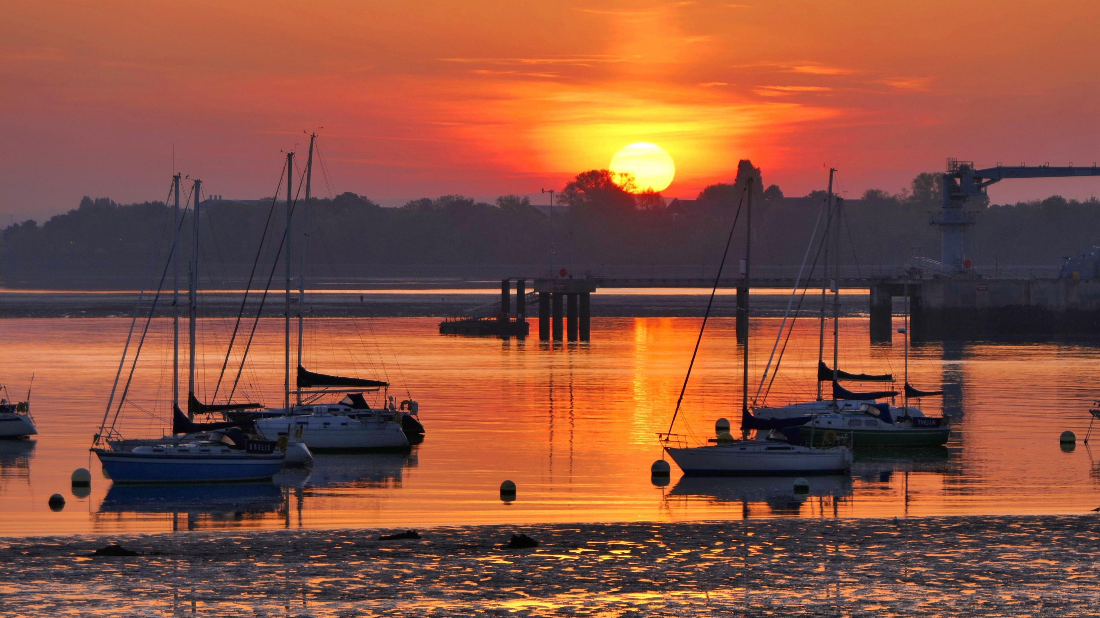 The sun is rising over Gosport harbour. You can see boats silhouetted in the foreground. The sky is glowing orange and reflecting in the water.