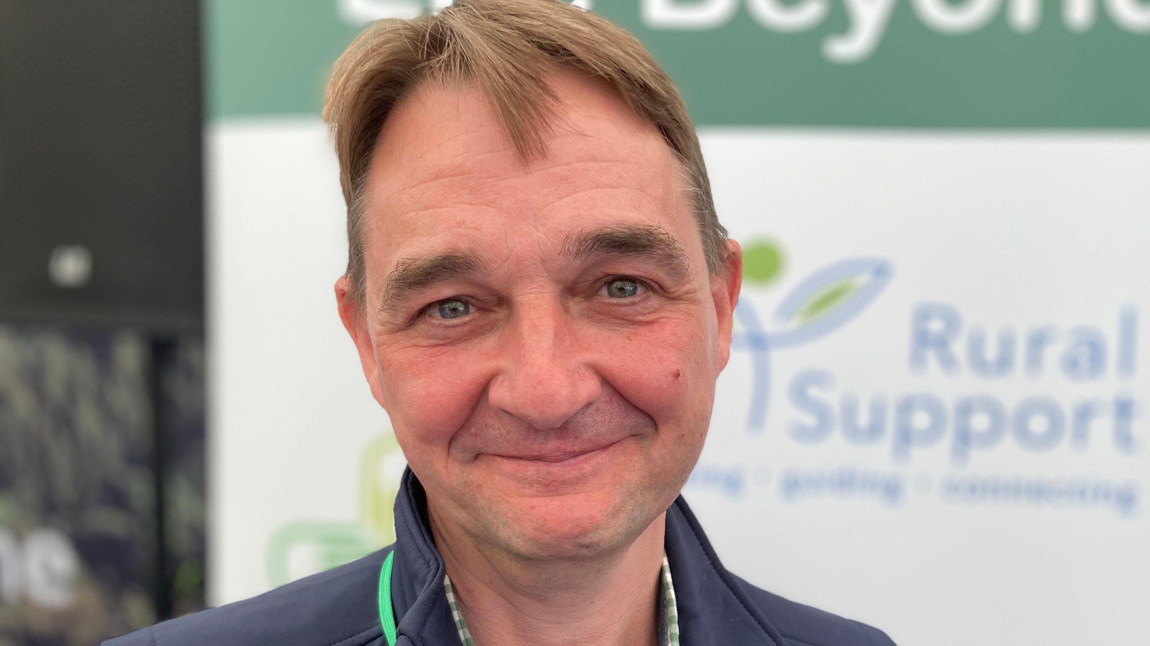 Head of Therapeutical Services and Crisis Support at Rural Support, Gyles Dawson standing in front of Rural Support branding at the Balmoral show 