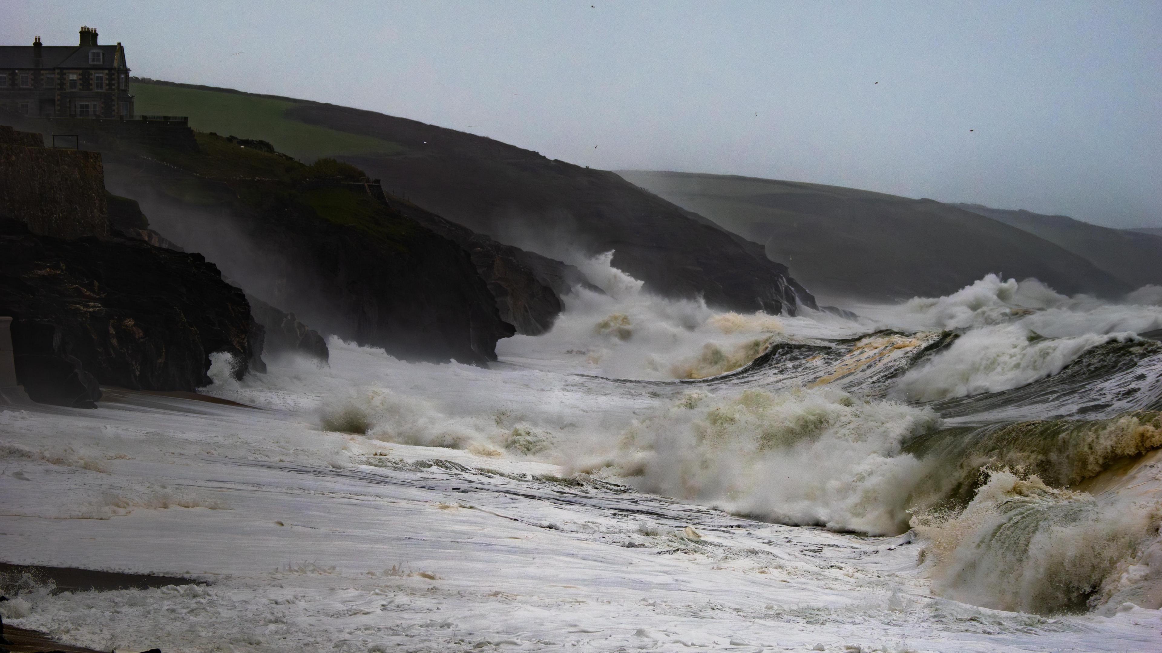 Waves crash on to a beach with rolling cliffs in the background.