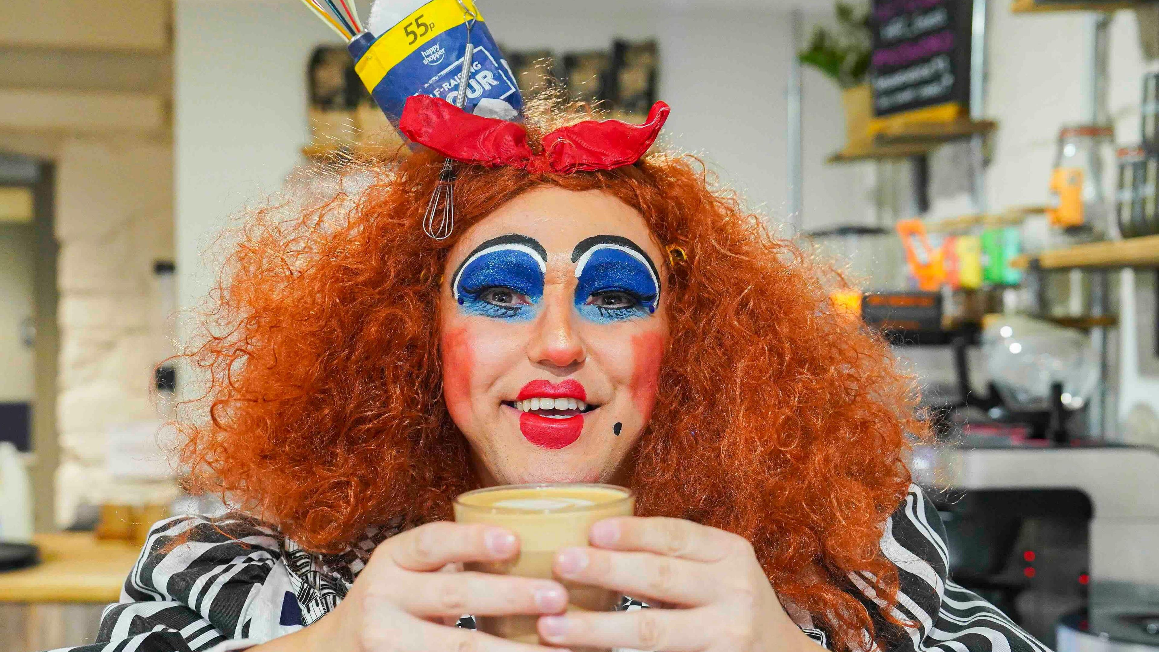 A pantomime date with a cup of tea in a glass and wearing a red wig and black and white striped top.