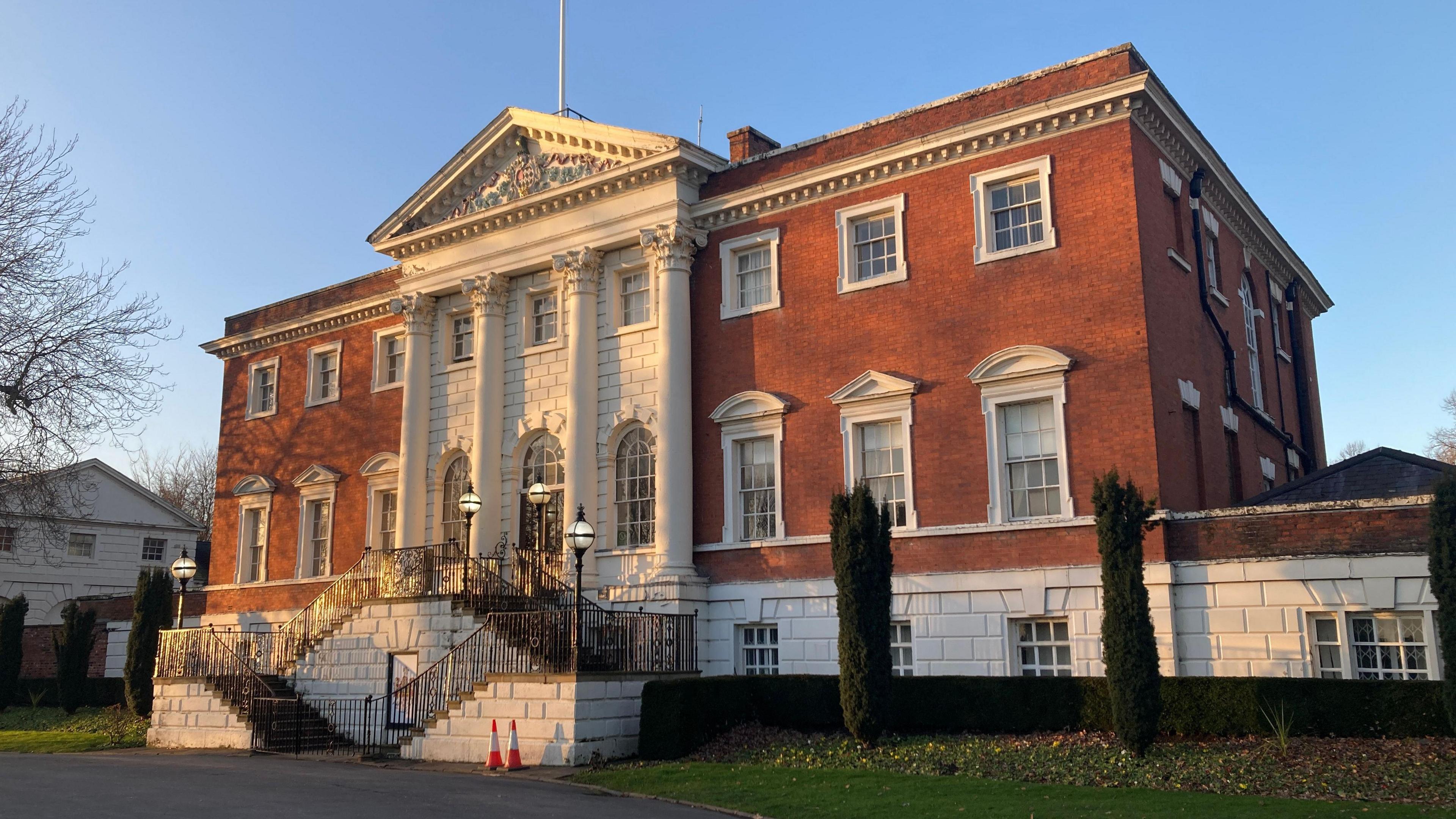 Warrington Town Hall is a large and imposing three-storey building mainly constructed from red bricks. At the centre of the building are three white columns leading up to a triangular pediment.