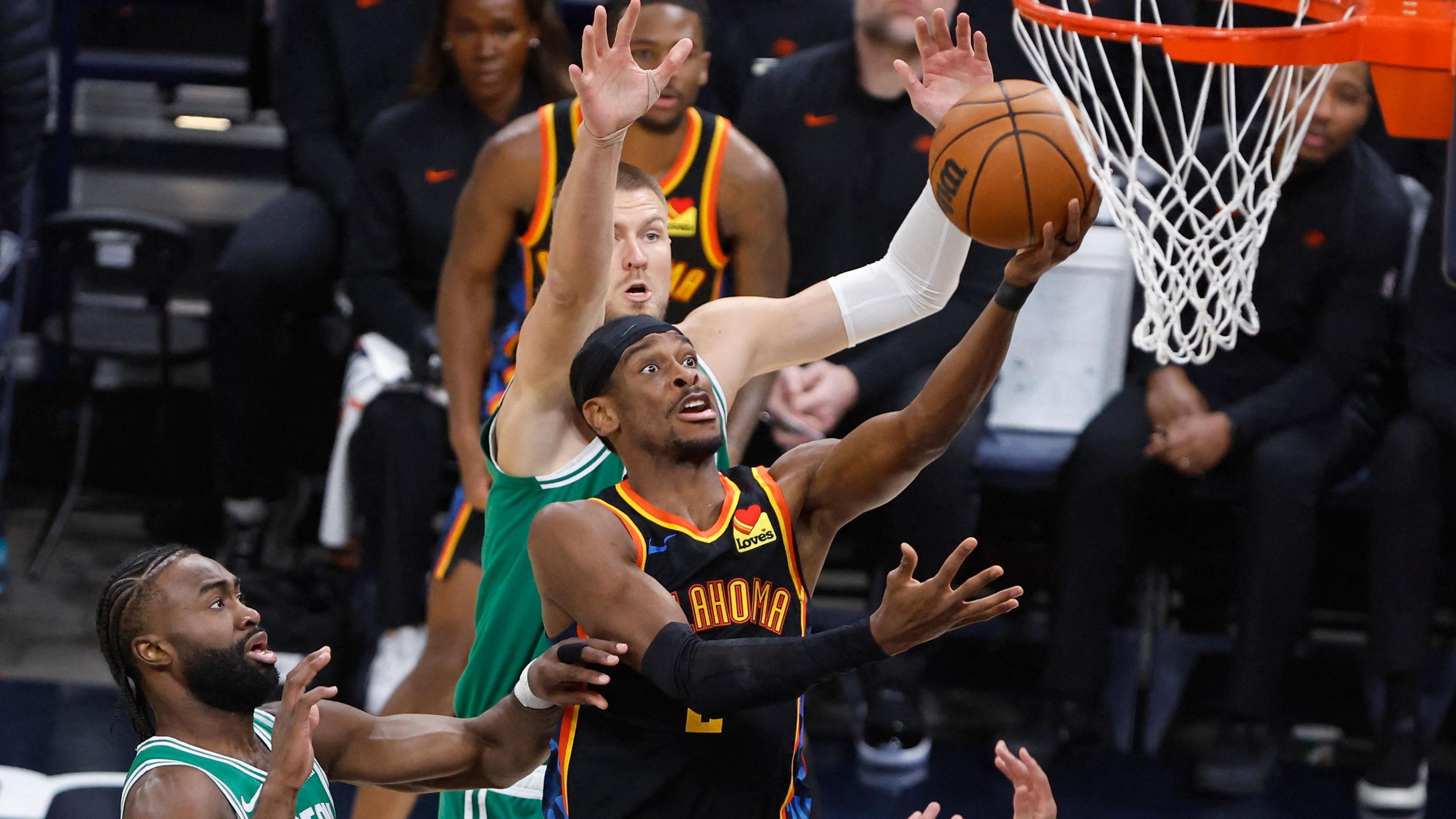 Shai Gilgeous-Alexander shooting a basket above three Boston players