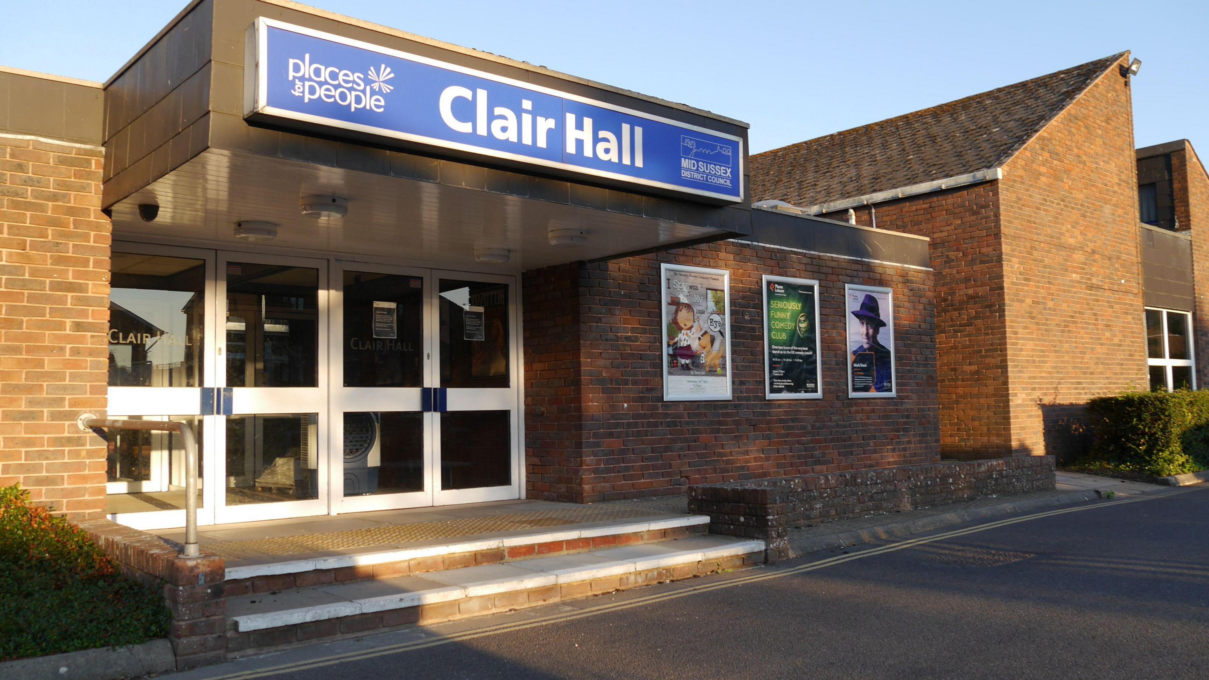 A brick community building with white doors and a blue sign that says Clair Hall. 