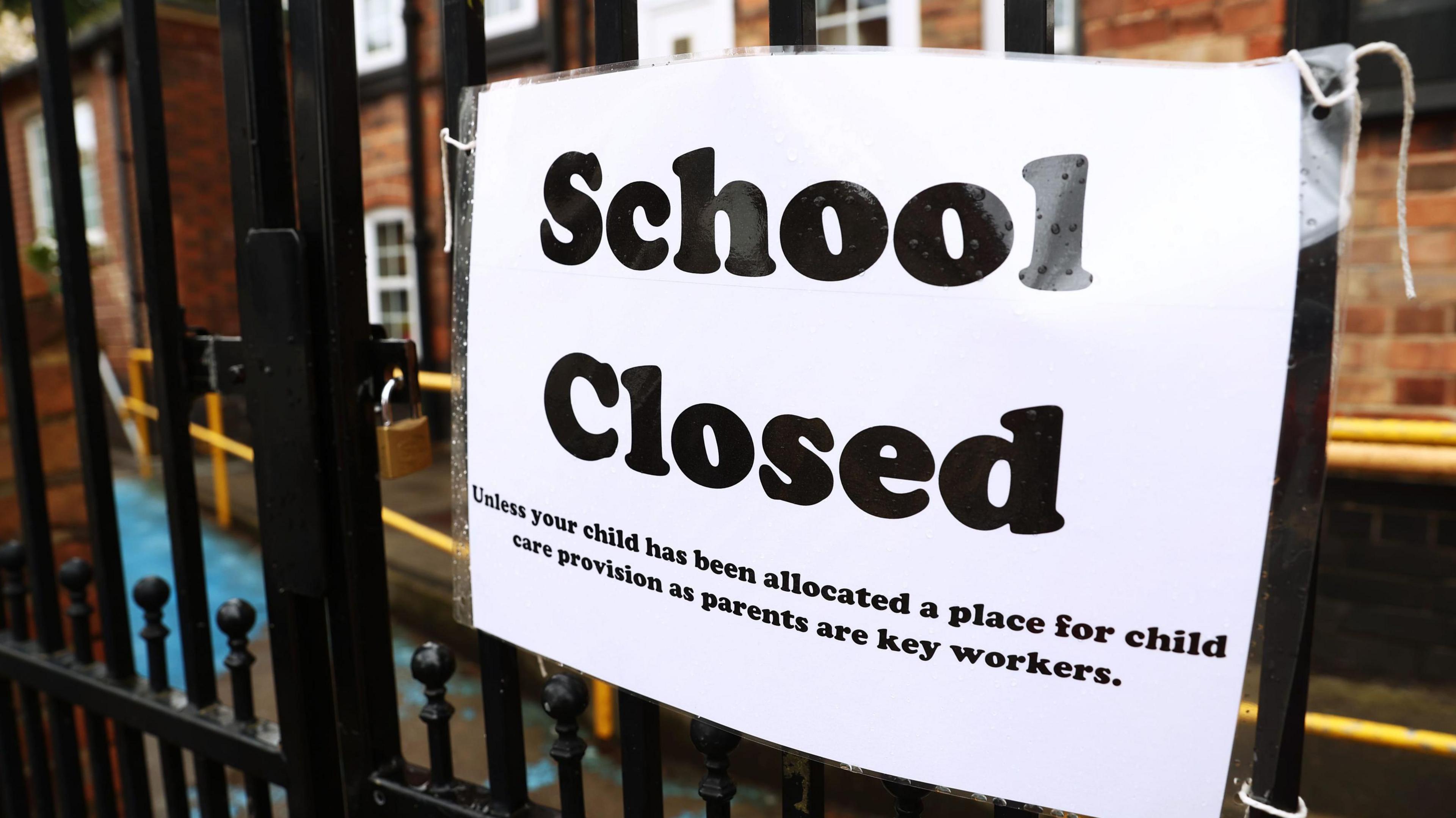 A black iron school gate with a notice attached to it stating "Closed - unless your child has been allocated a place for child care provision as parents are key workers"