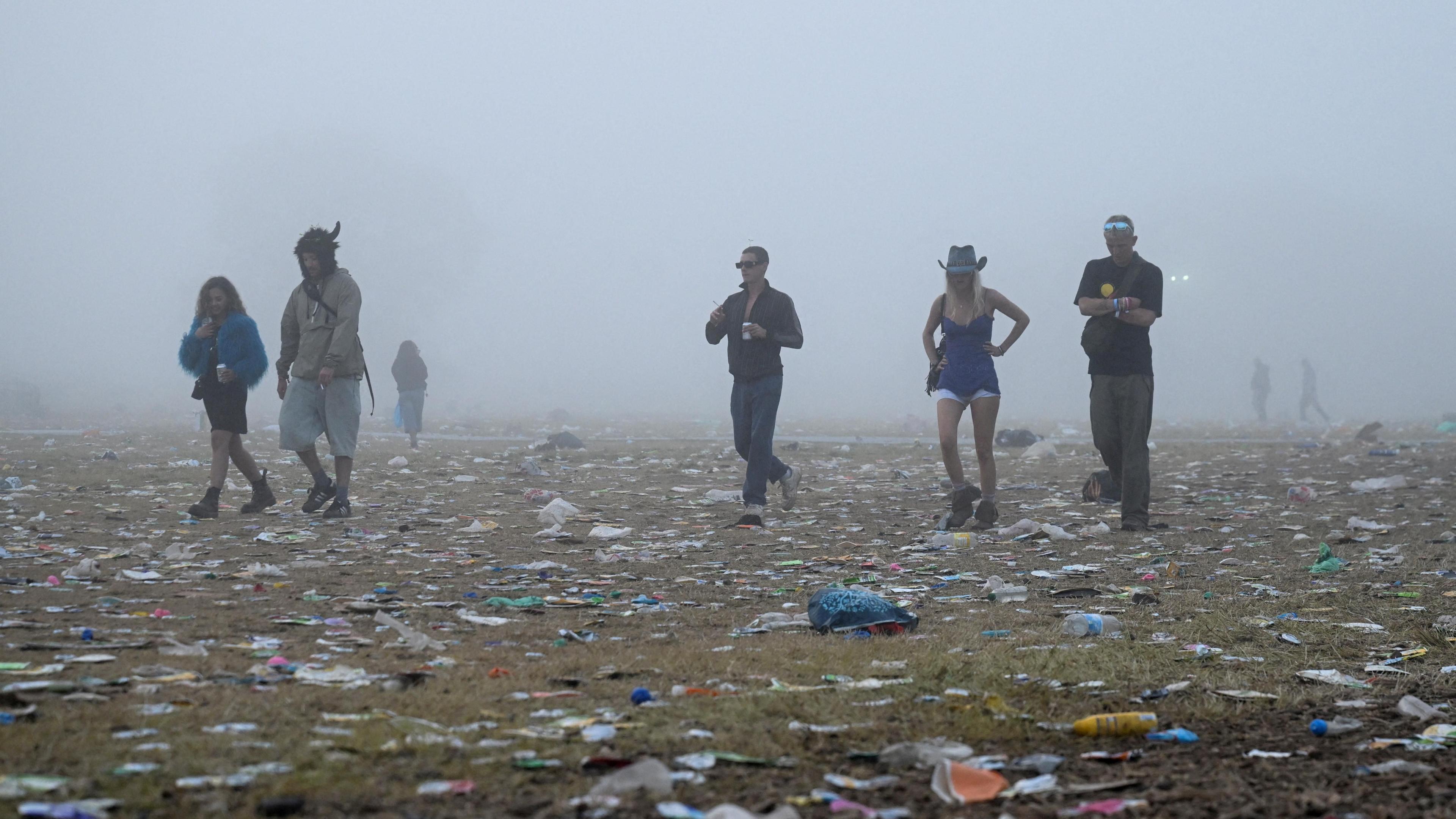 People are walking across a field with litter scattered across. It is foggy.